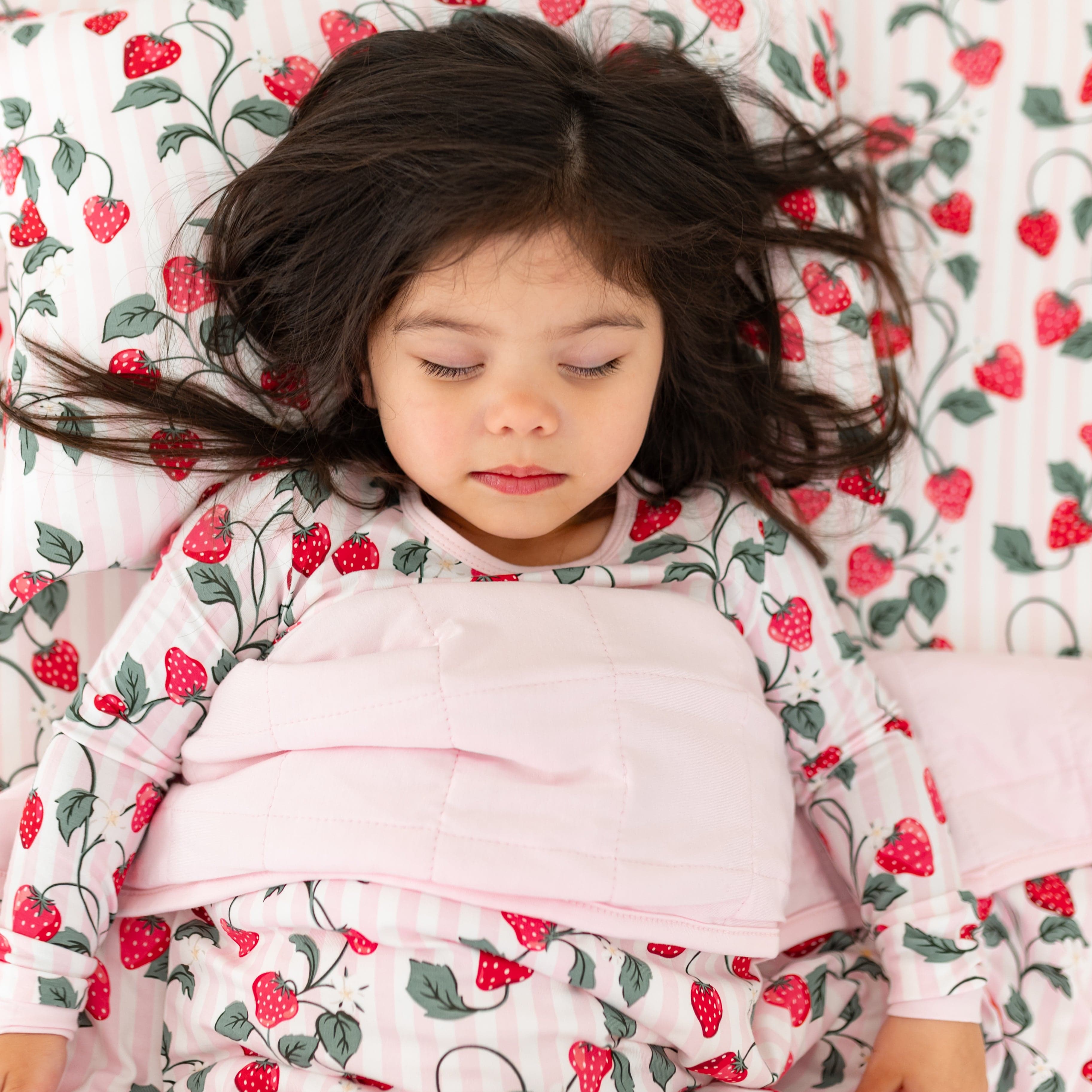 Young girl sleeping in bed with the Toddler Blanket in Strawberry Fields 1.0 overtop of her laying on a pillow with a Toddler Pillowcase in Strawberry Fields on it