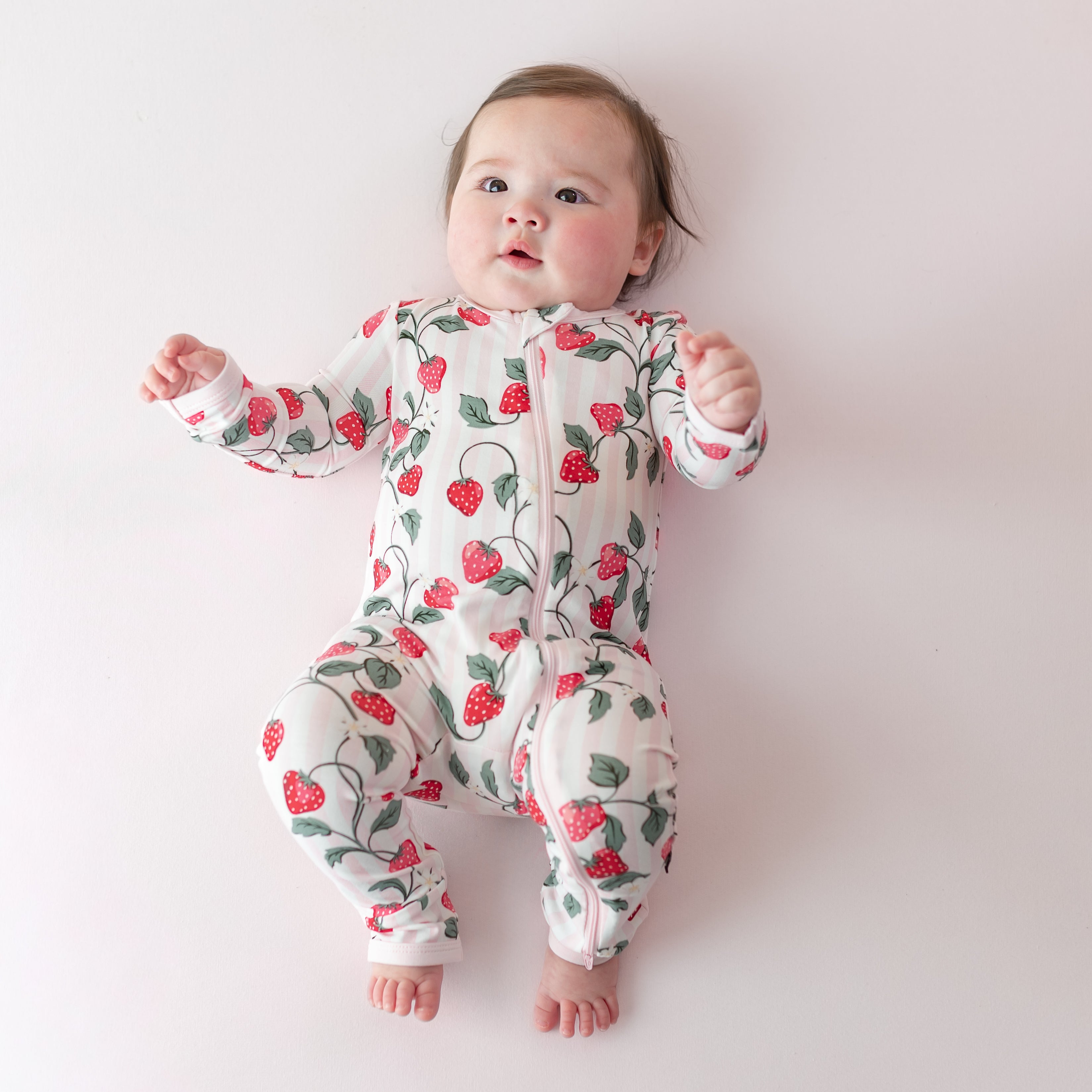 Infant laying on a light pink surface wearing the Zippered Romper in Strawberry Fields