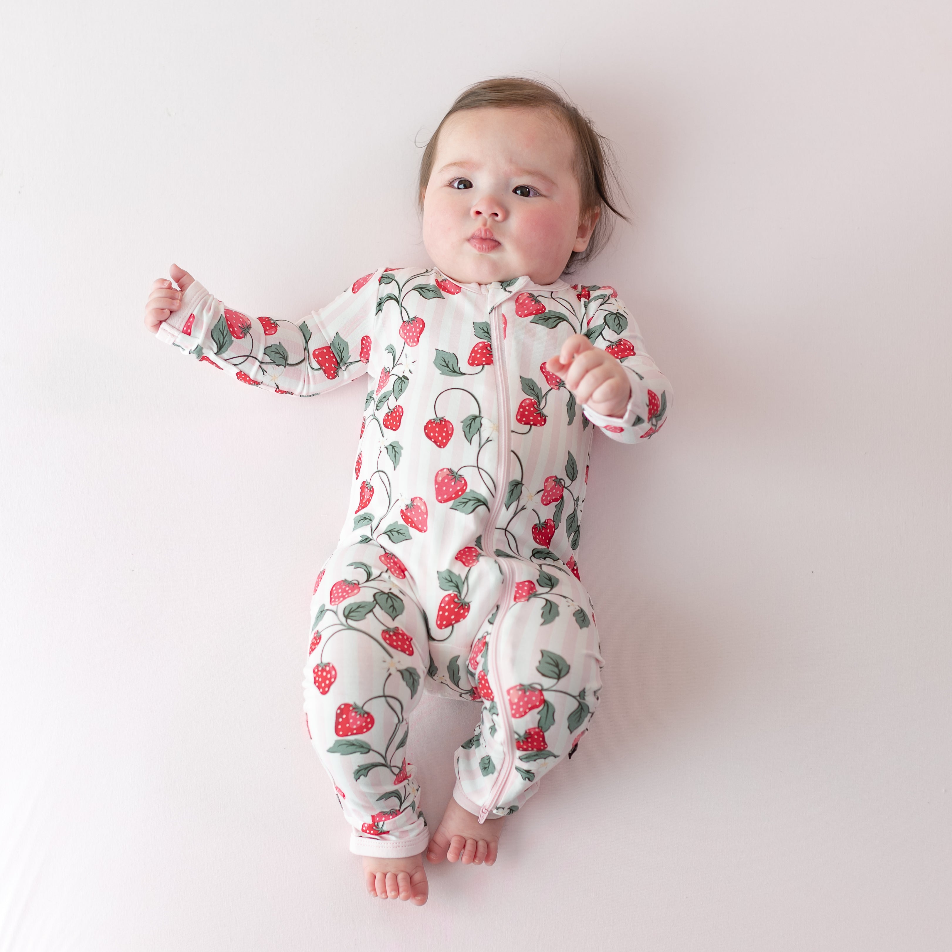 Infant laying on a light pink surface wearing the buttery soft Zippered Romper in Strawberry Fields