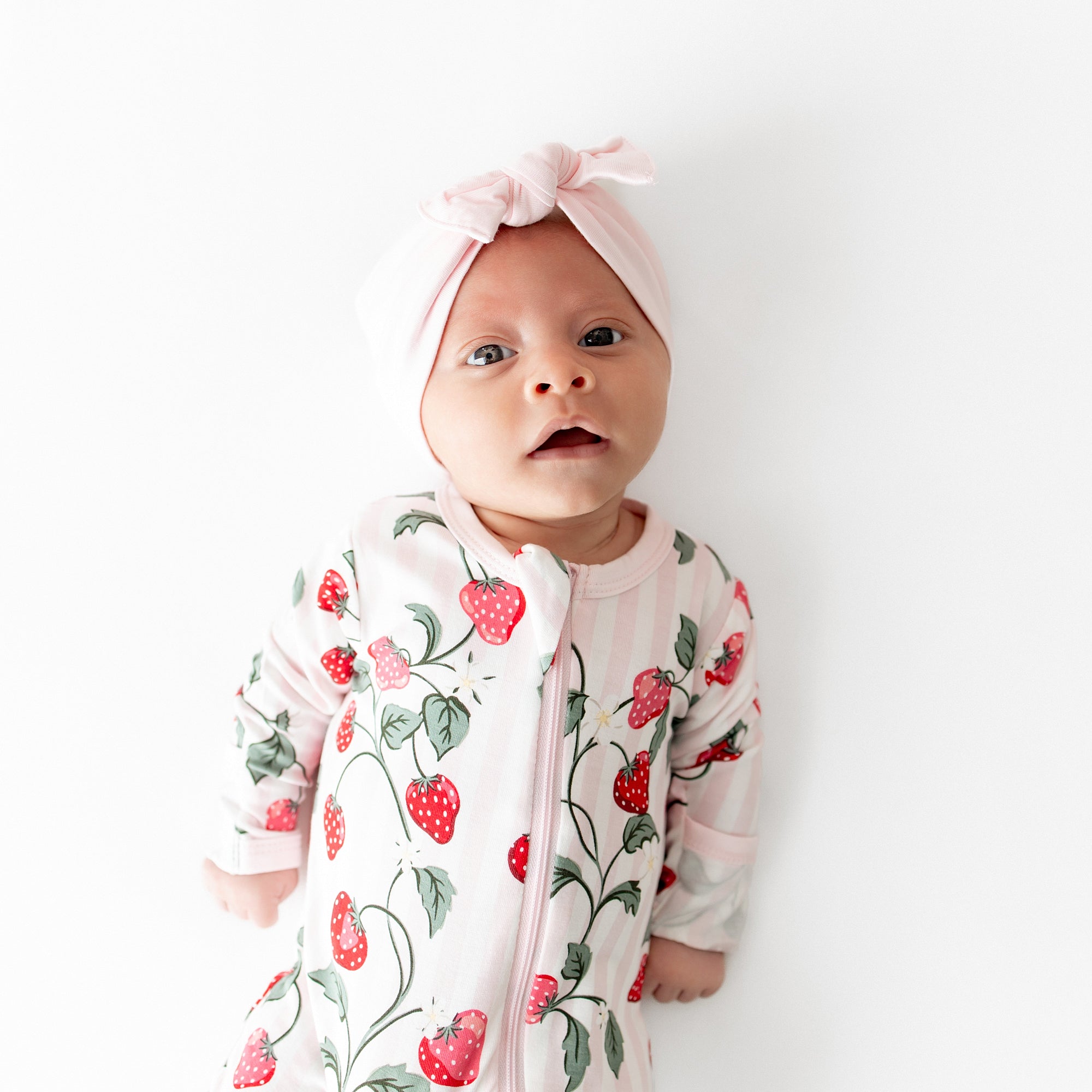 Close up of newborn wearing the Zippered Footie in Strawberry Fields with a pink knotted bow