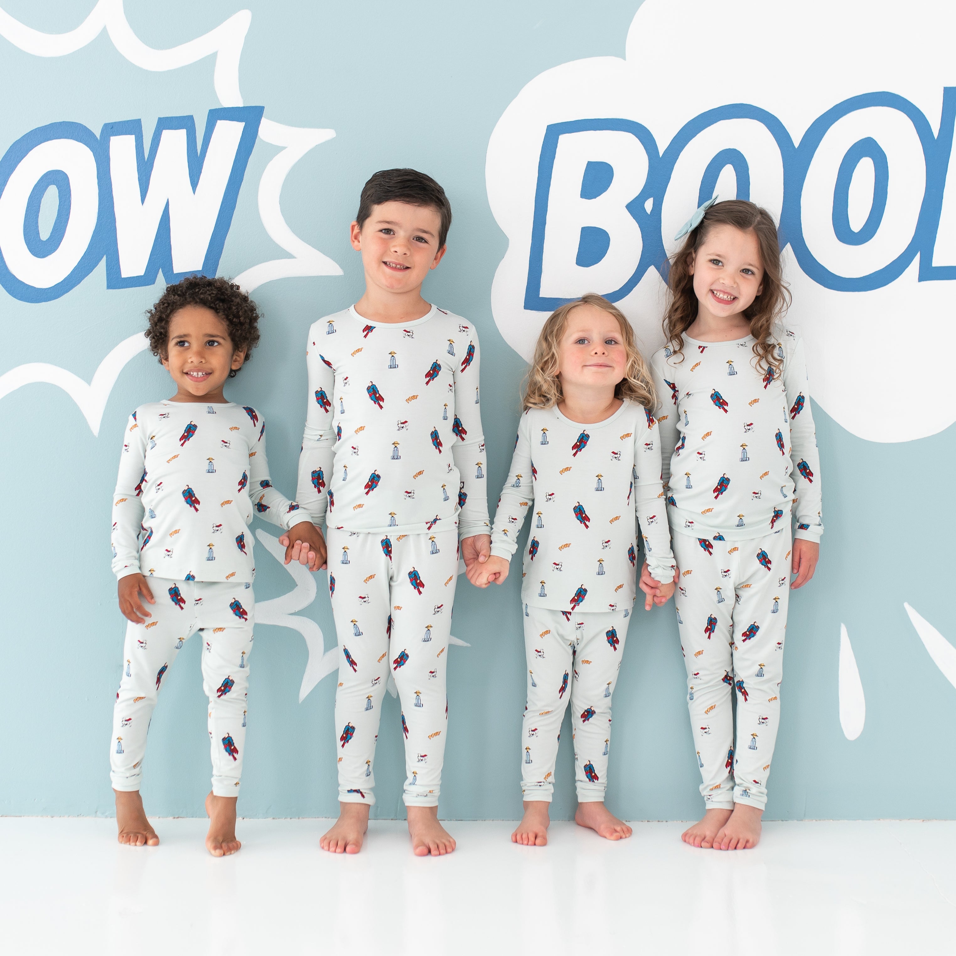Four child models standing holding hands wearing the Long Sleeve Pajamas in Superman™
