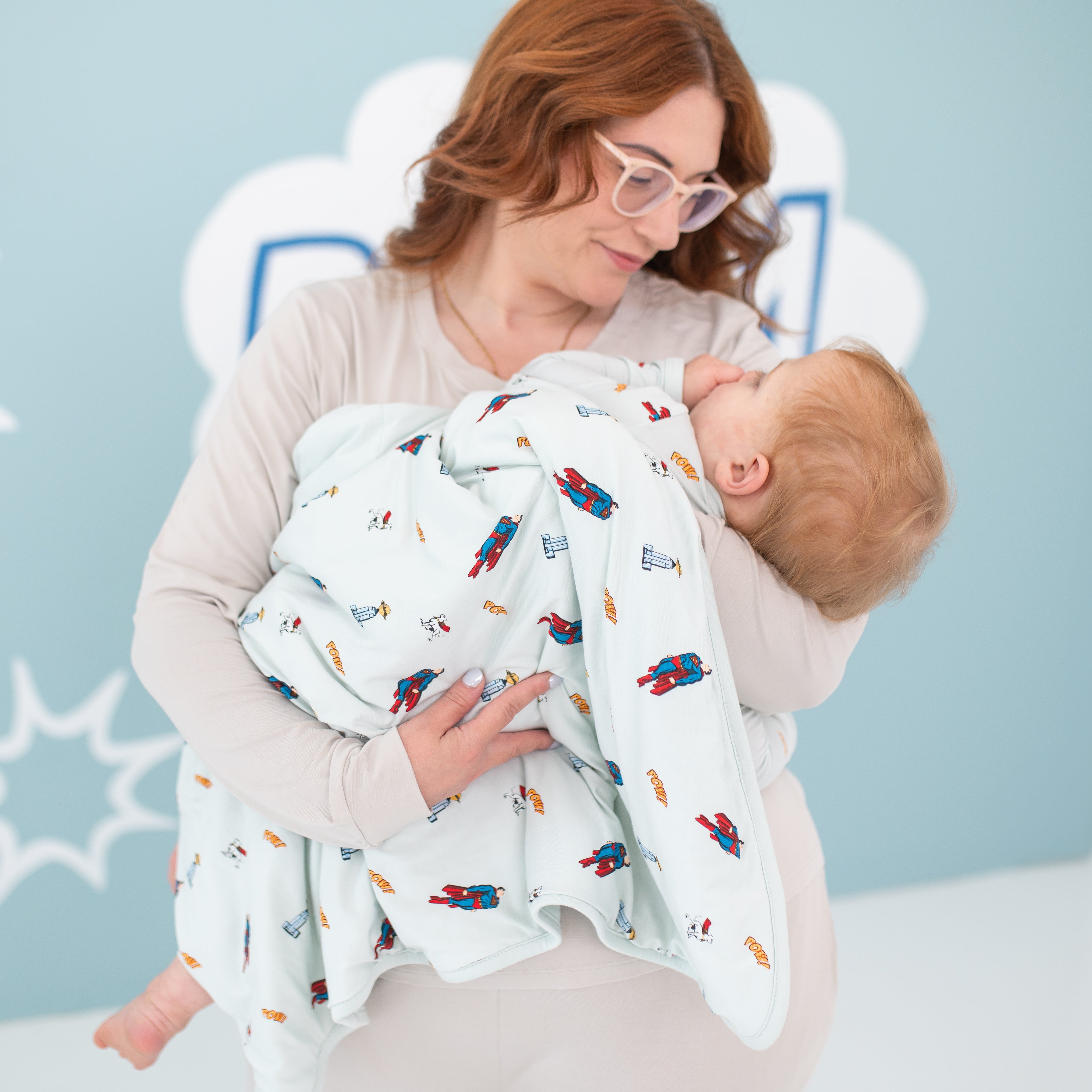 Mother holding toddler wrapped in the Baby Blanket in Superman™ 1.0 TOG