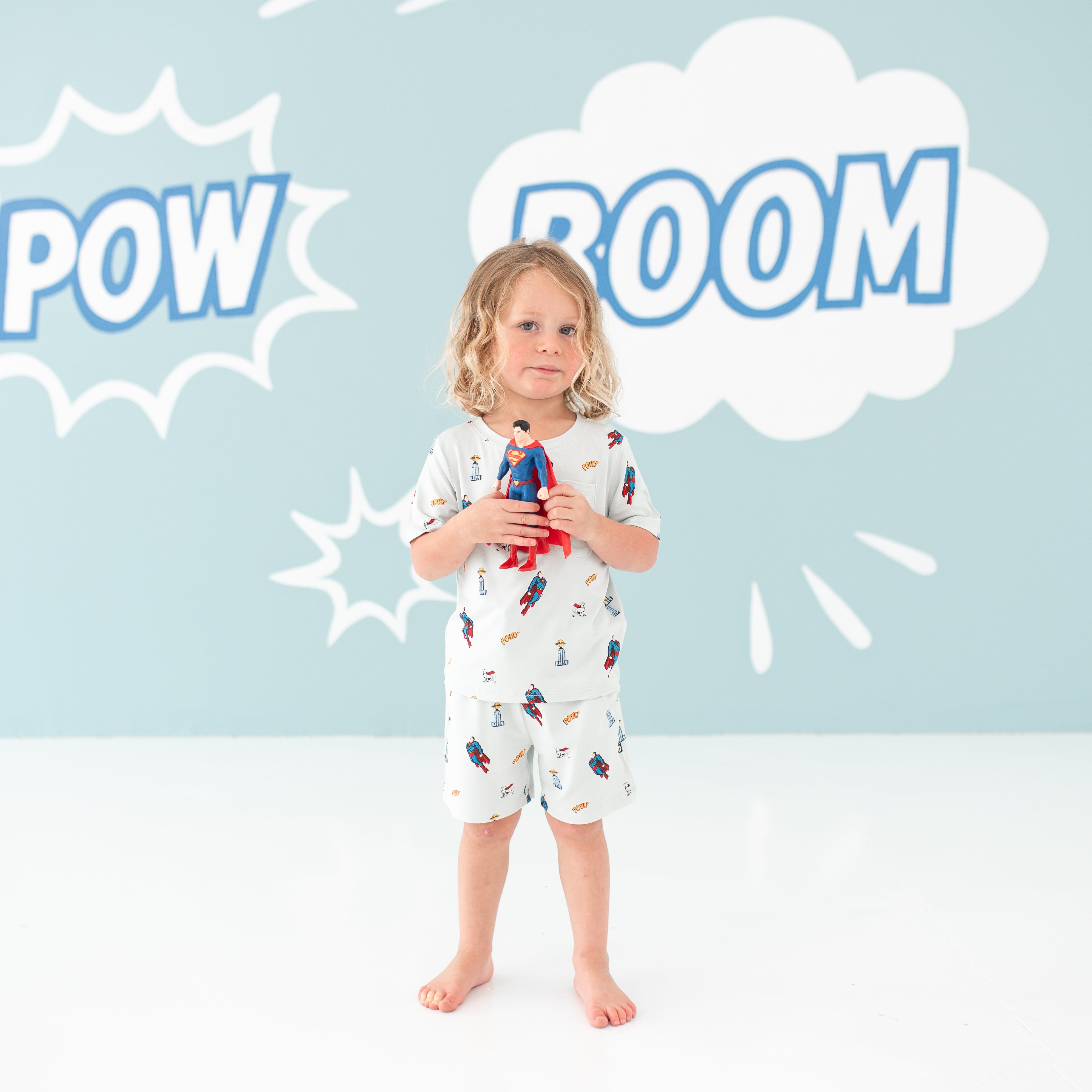 Child model holding a Superman action figure wearing the Drawstring Short in Superman™ and matching Crew Neck Tee