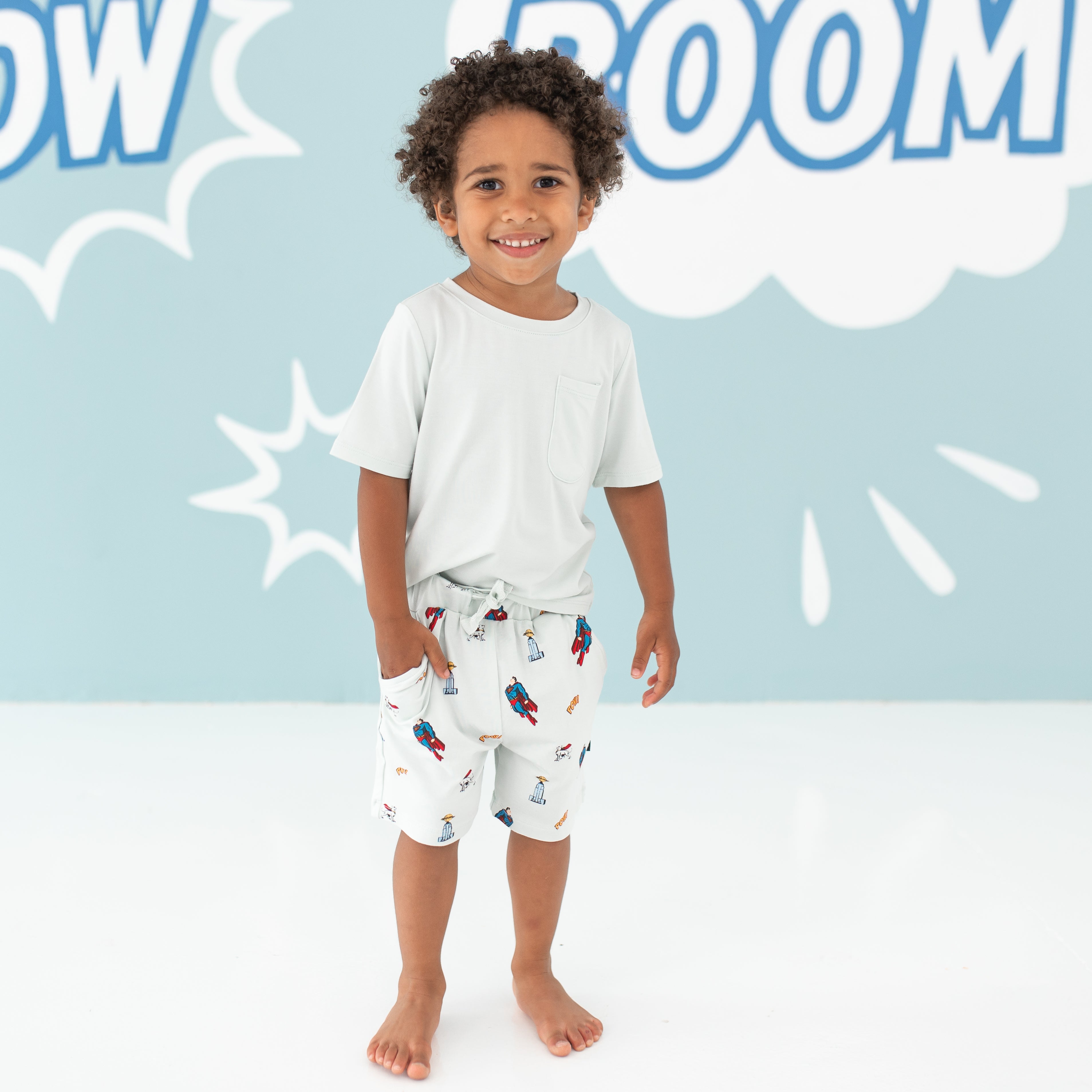 Child model standing with his hand in his Drawstring Short in Superman™ pocket paired with a Toddler Crew Neck Tee in Dew