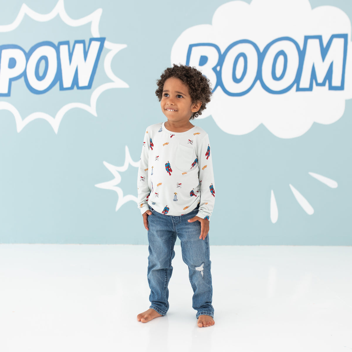 Smiling model wearing the Long Sleeve Toddler Crew Neck Tee in Superman™ paired with jeans