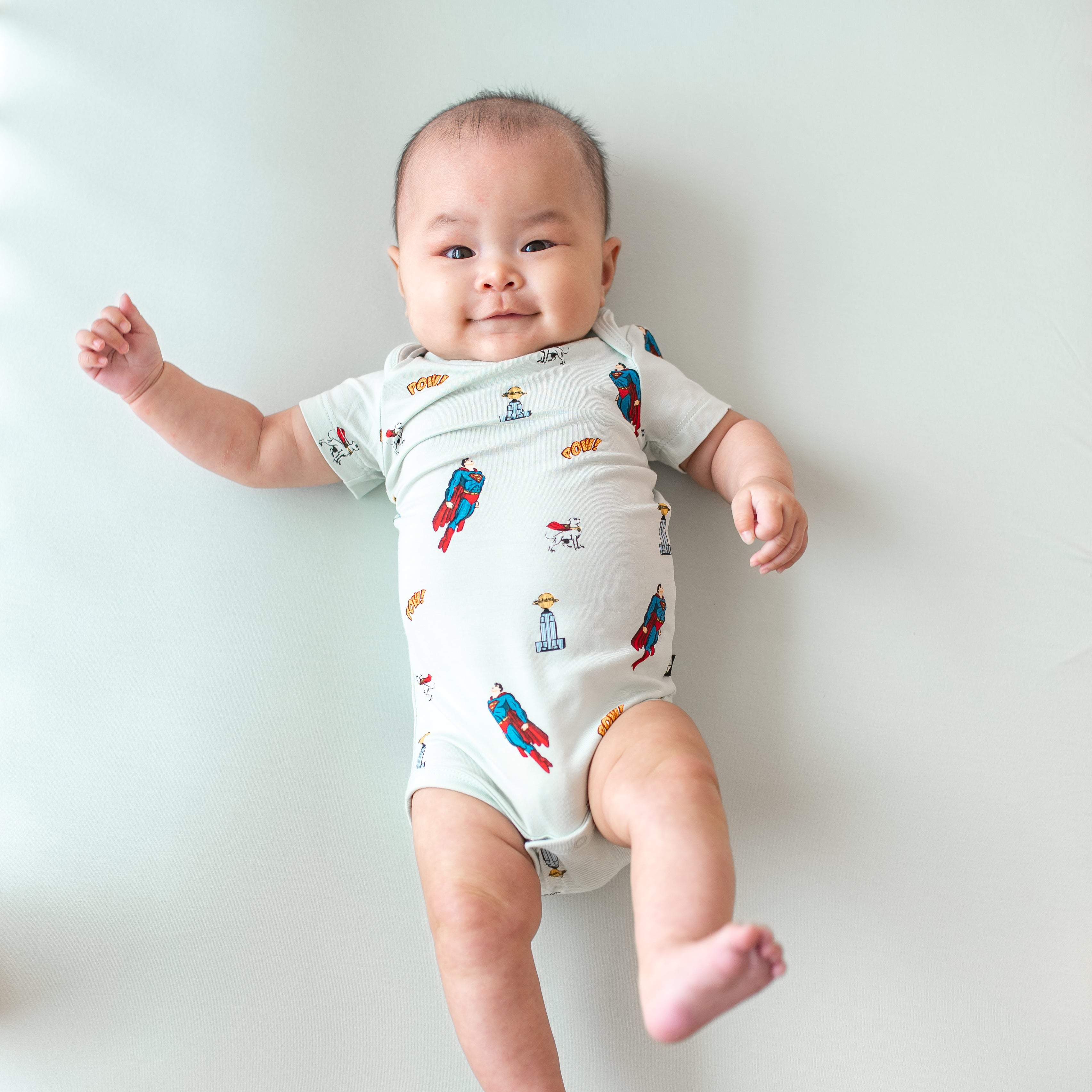 Infant model laying down wearing the Bodysuit in Superman™ with one leg up in the air