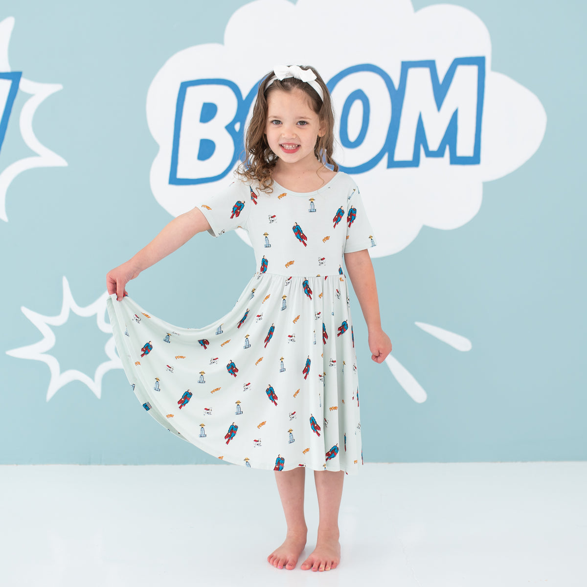 Young girl standing holding one side of her Twirl Dress in Superman™