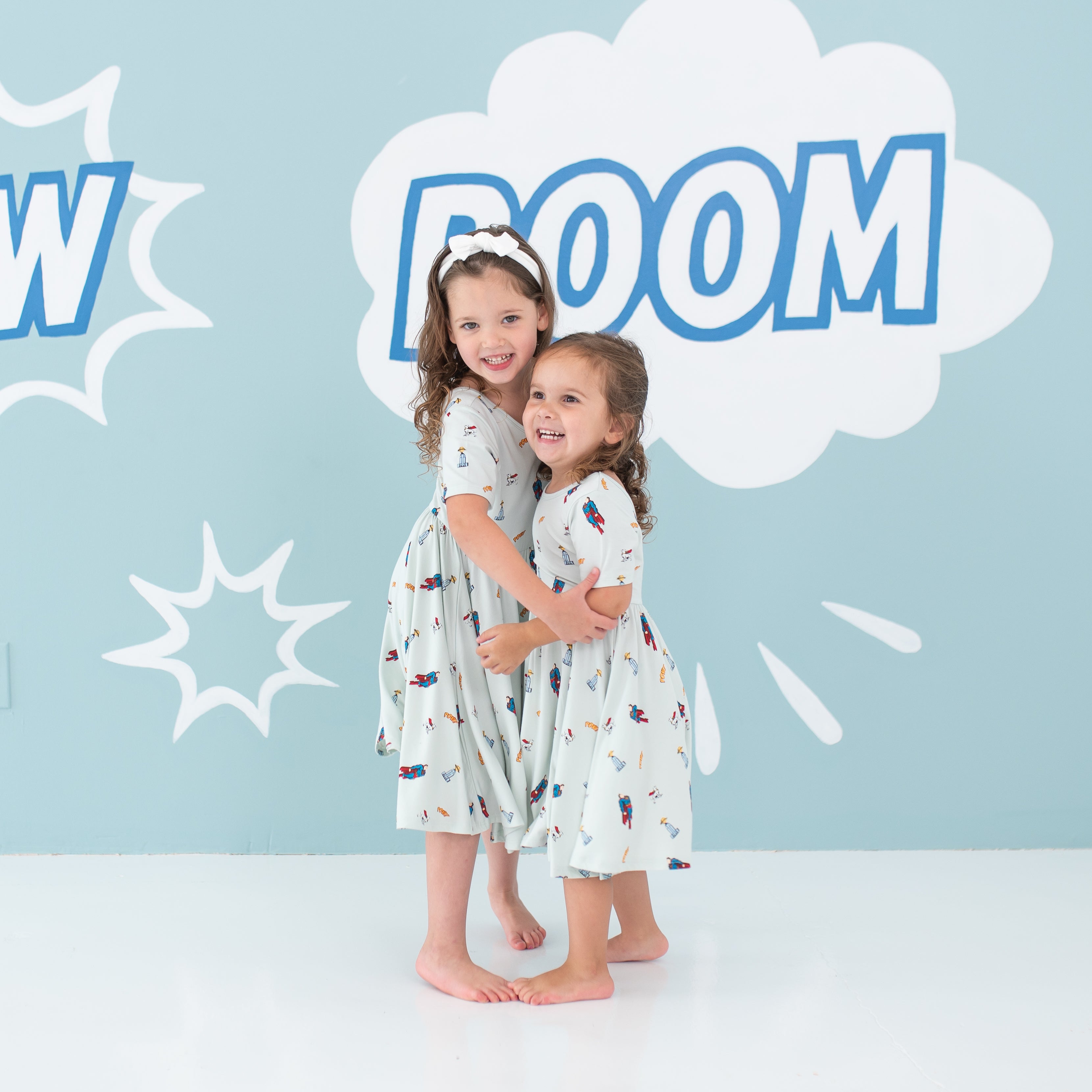 Two girl models hugging one another wearing the Twirl Dress in Superman™