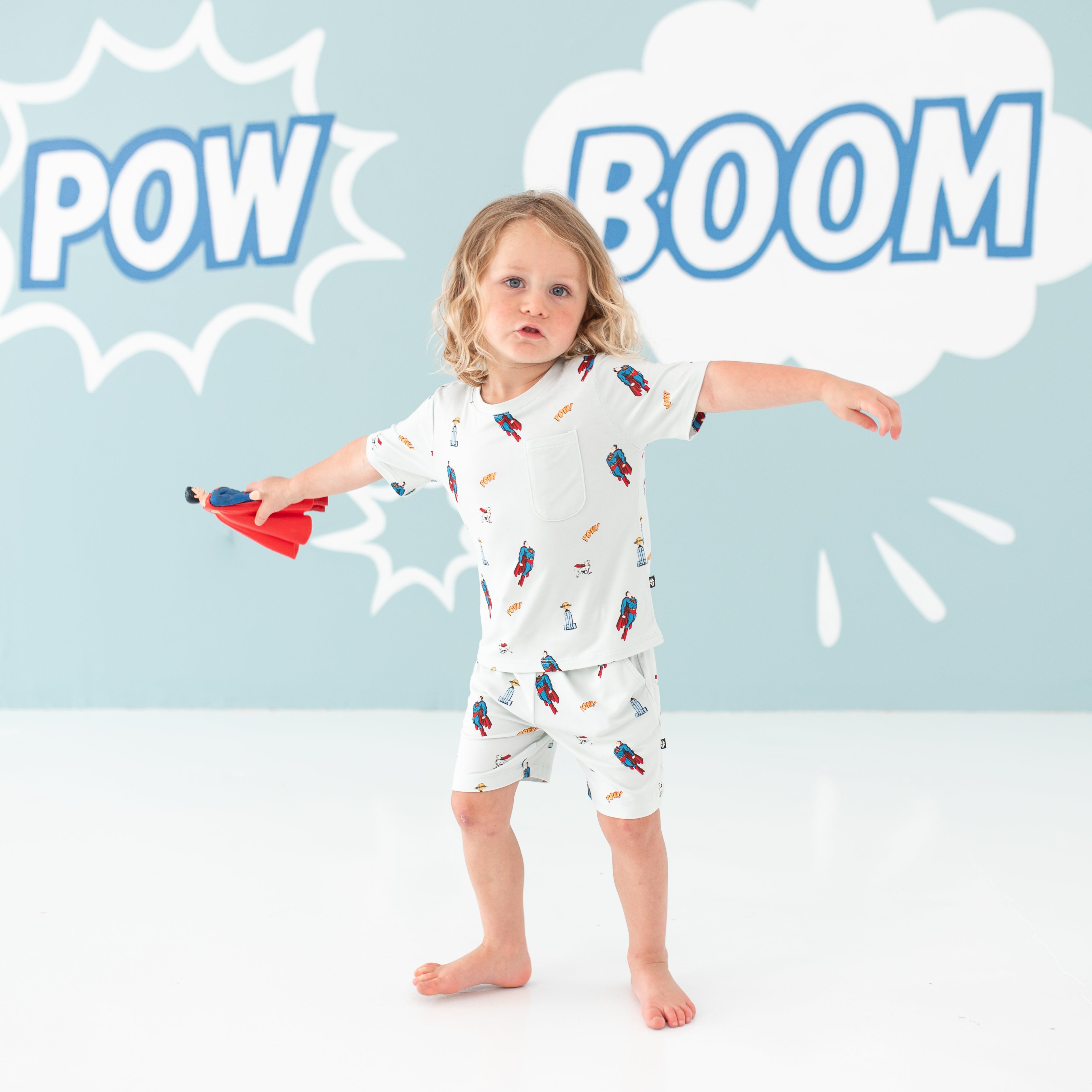 Toddler spinning holding a Superman action figure wearing the Toddler Crew Neck Tee in Superman™ and matching drawstring shorts