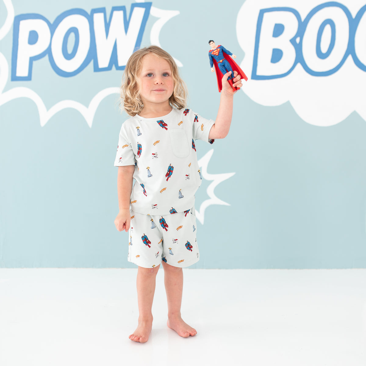 Toddler standing holding a superman action figure with one hand wearing the Toddler Crew Neck Tee in Superman™ paired with the matching drawstring shorts