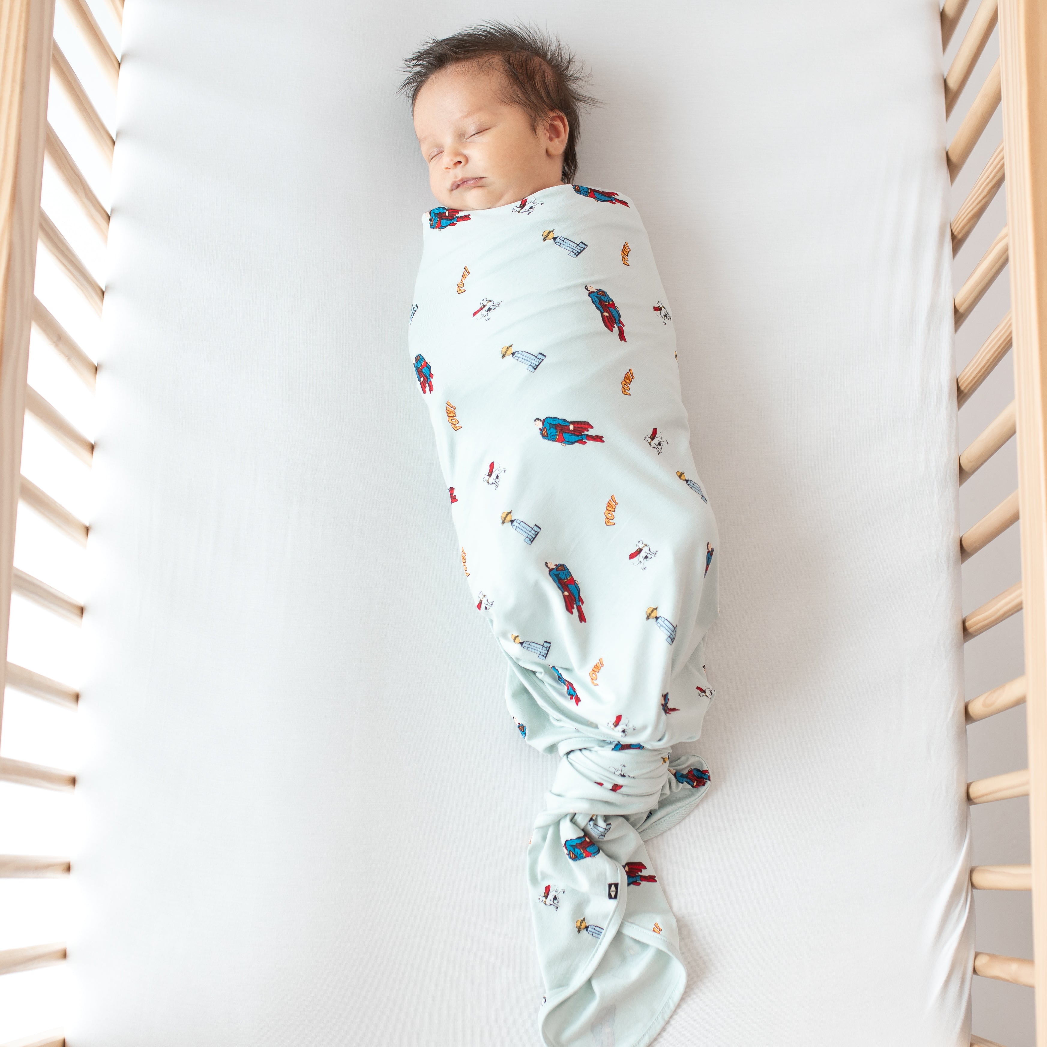 Sleeping newborn laying in a crib swaddled in the Swaddle Blanket in Superman™