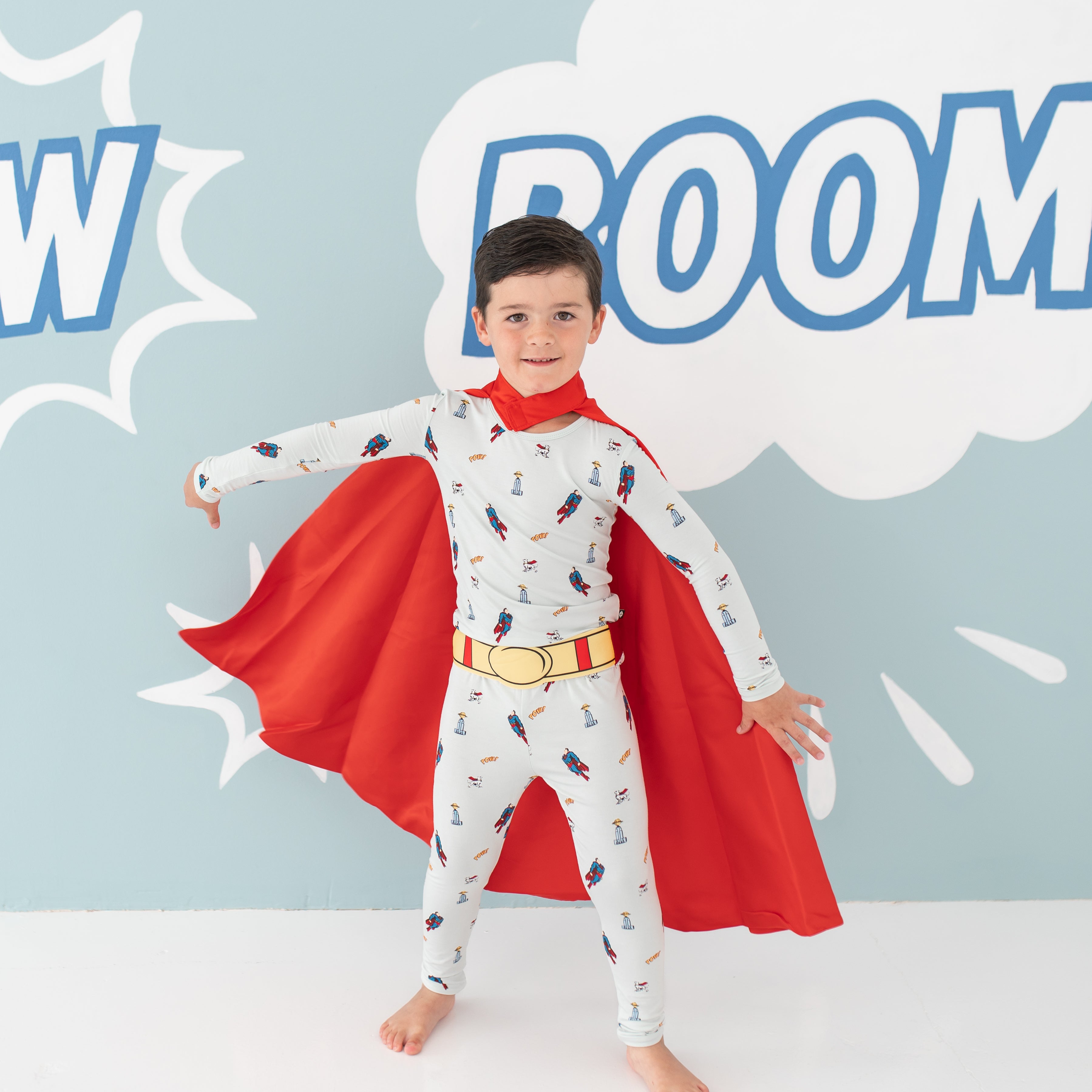 Kid wearing the Long Sleeve Pajamas in Superman™ with a red cape and red and yellow belt
