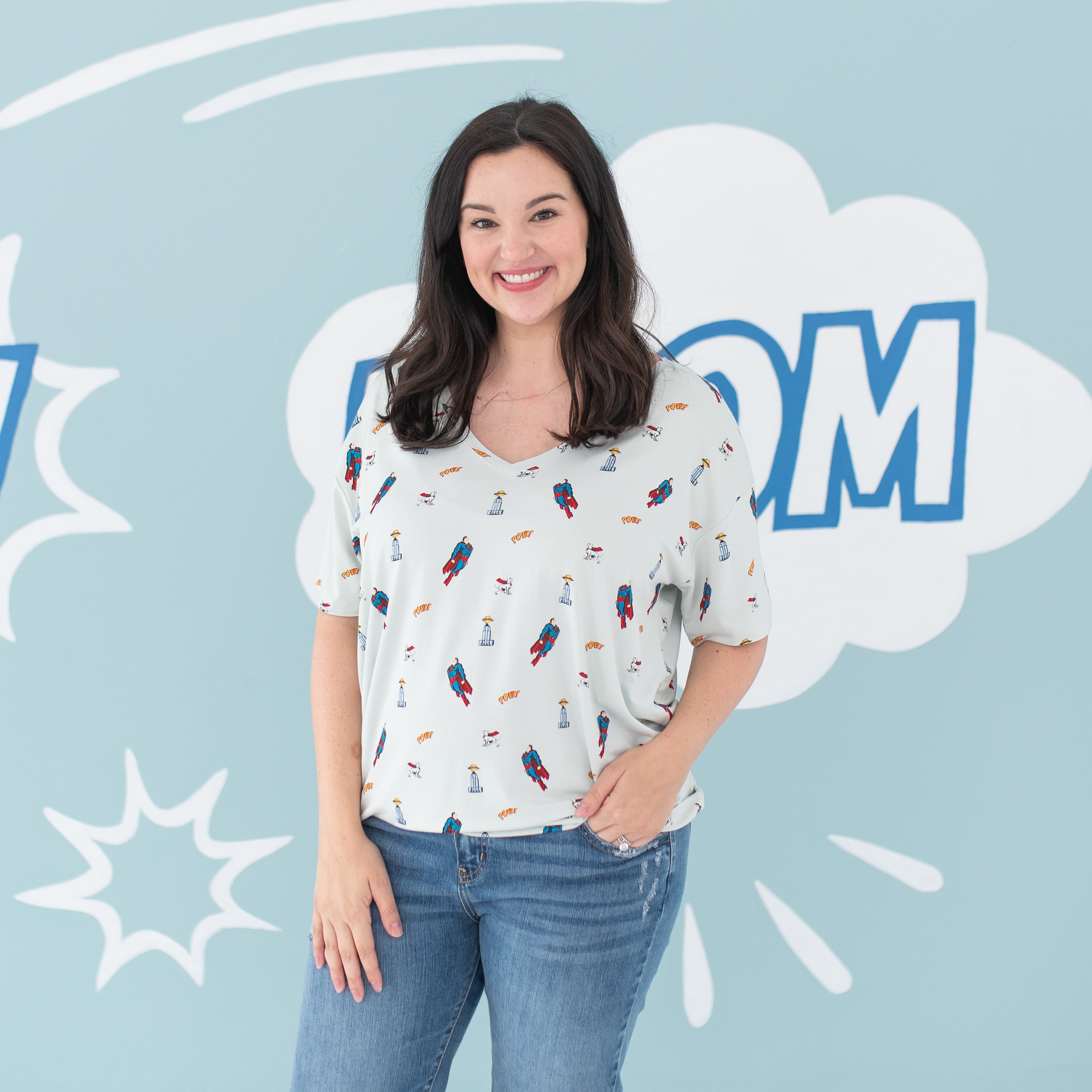Smiling female model wearing the Women's Relaxed Fit V-Neck in Superman™ paired with medium wash jeans