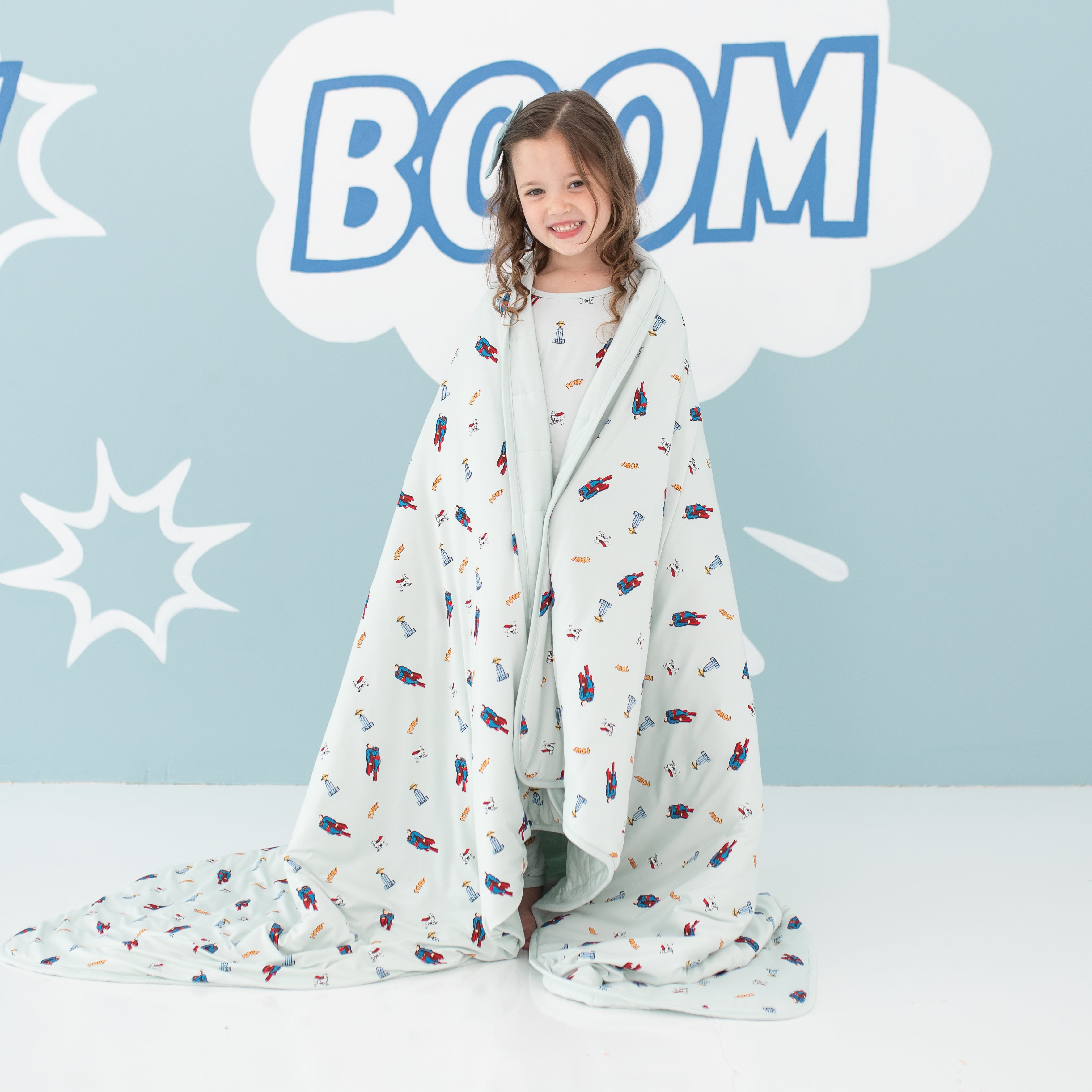 Smiling girl standing with the Youth Blanket in Superman™ 2.5 wrapped around her