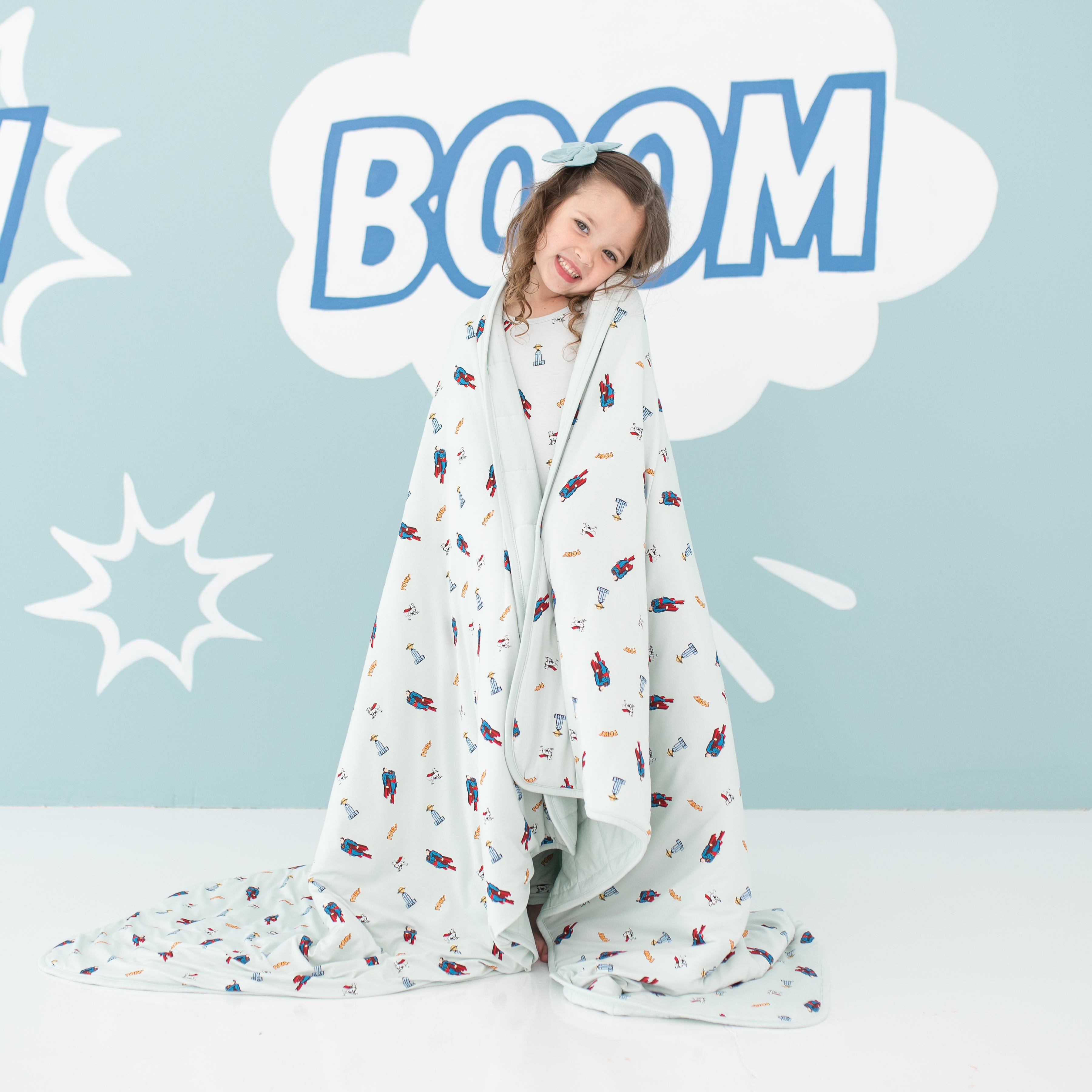Smiling girl with head tilted to the side standing with the Youth Blanket in Superman™ 2.5 wrapped around her