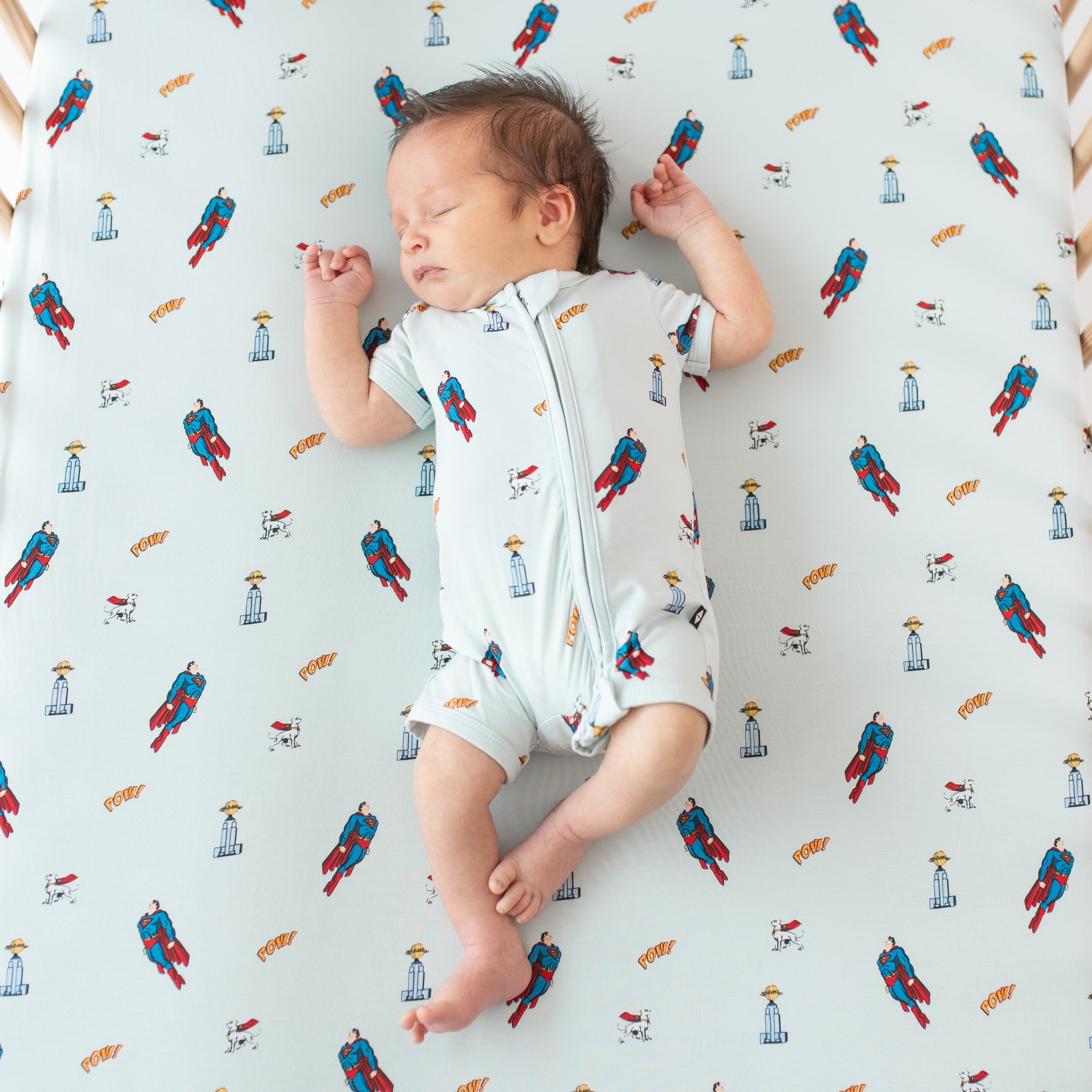 Newborn sleeping in a crib on a Crib Sheet in Superman™ wearing a matching Zippered Shortall