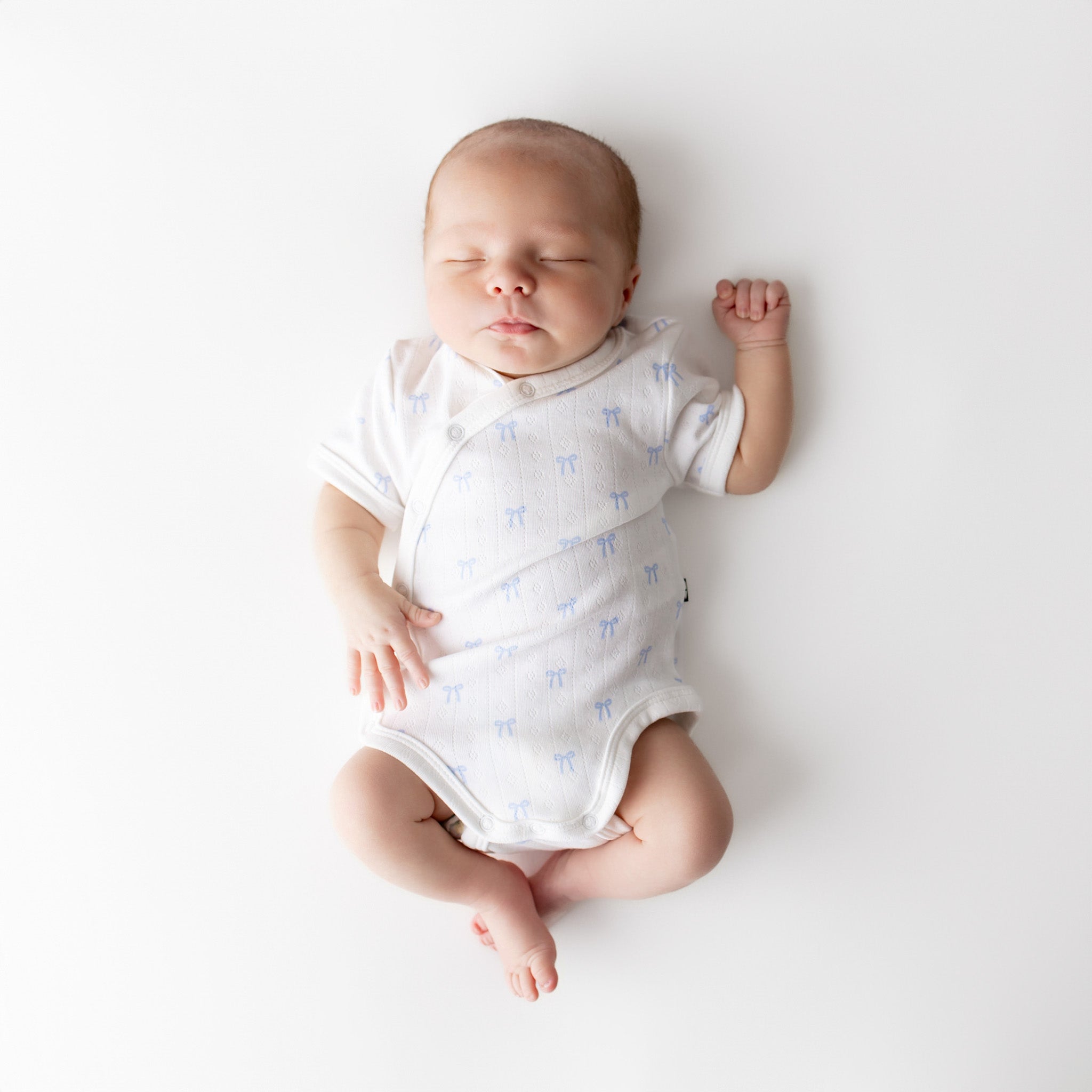 Newborn baby in a white onesie with blue patterns on a light gray background