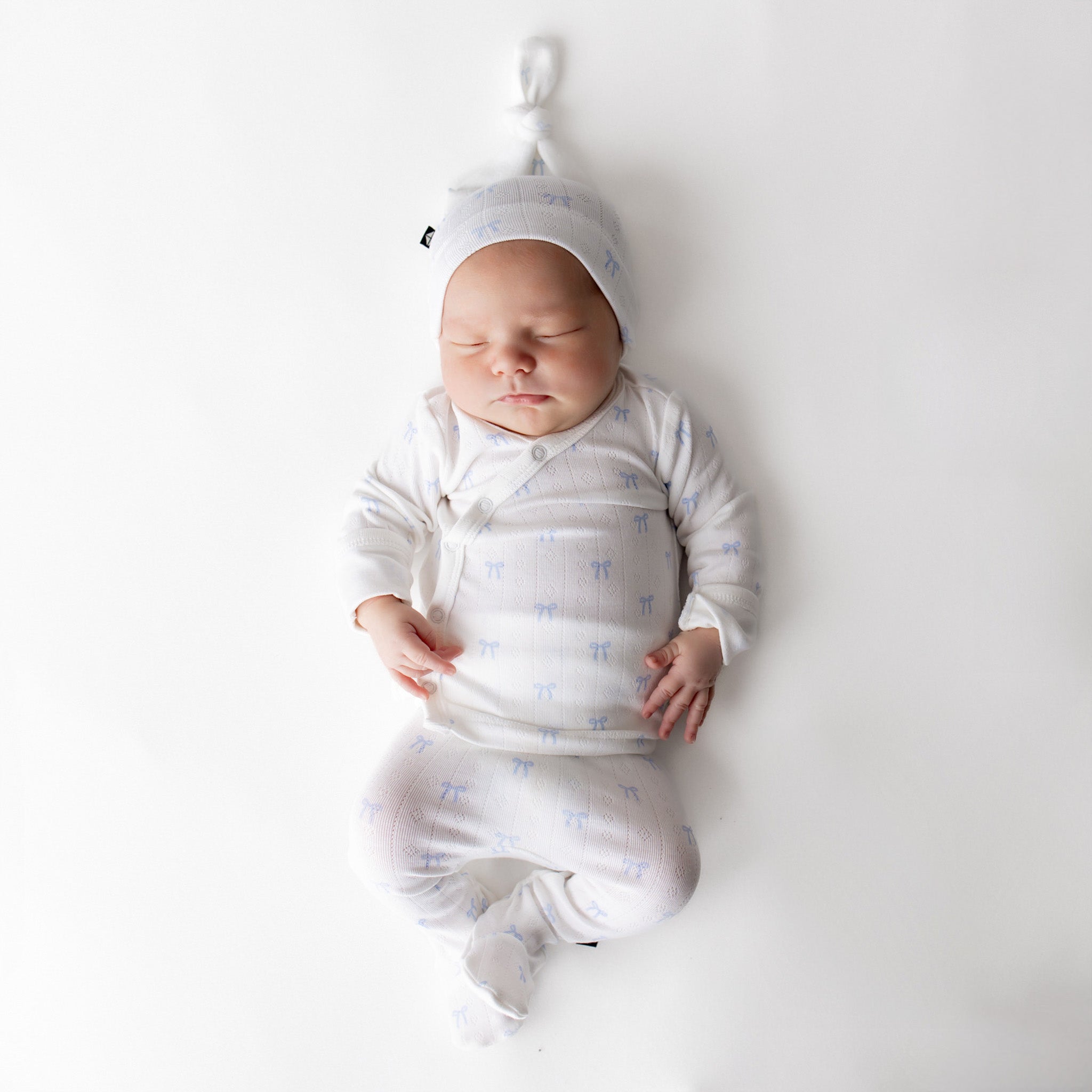 Newborn baby in a white outfit with blue patterns, lying on a white background