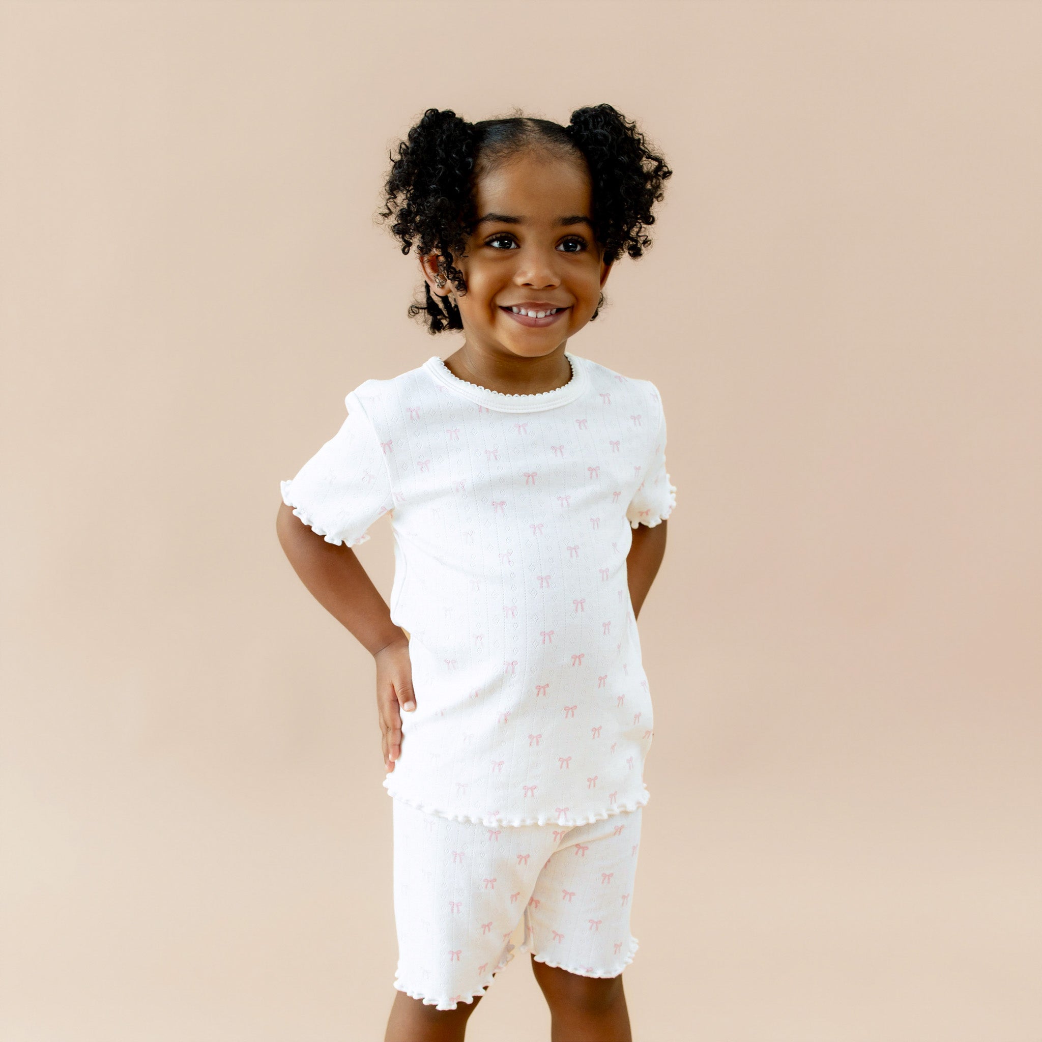 Young girl wearing a white outfit with ruffled sleeves and shorts on a beige background