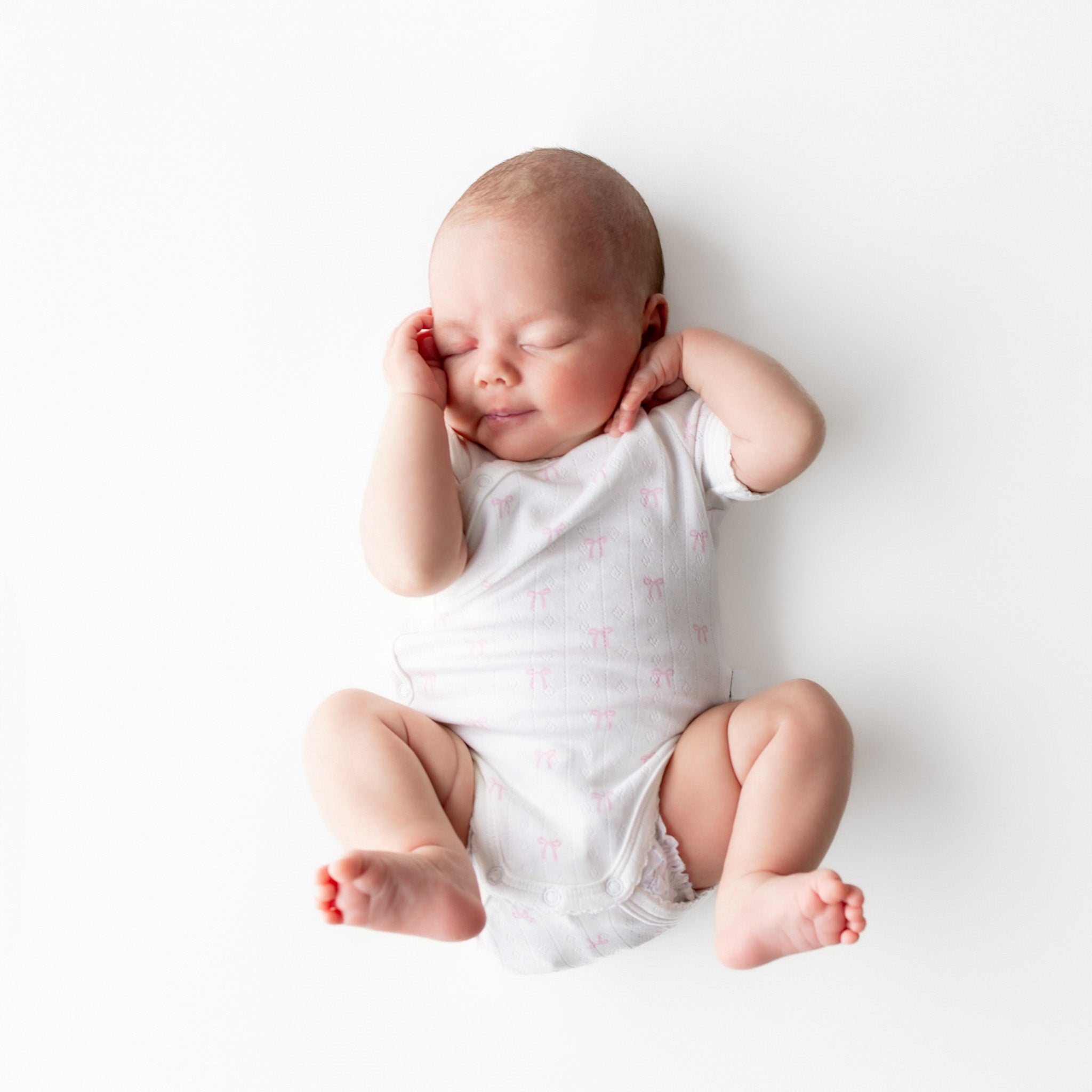 Newborn baby in a white onesie with pink patterns on a white background