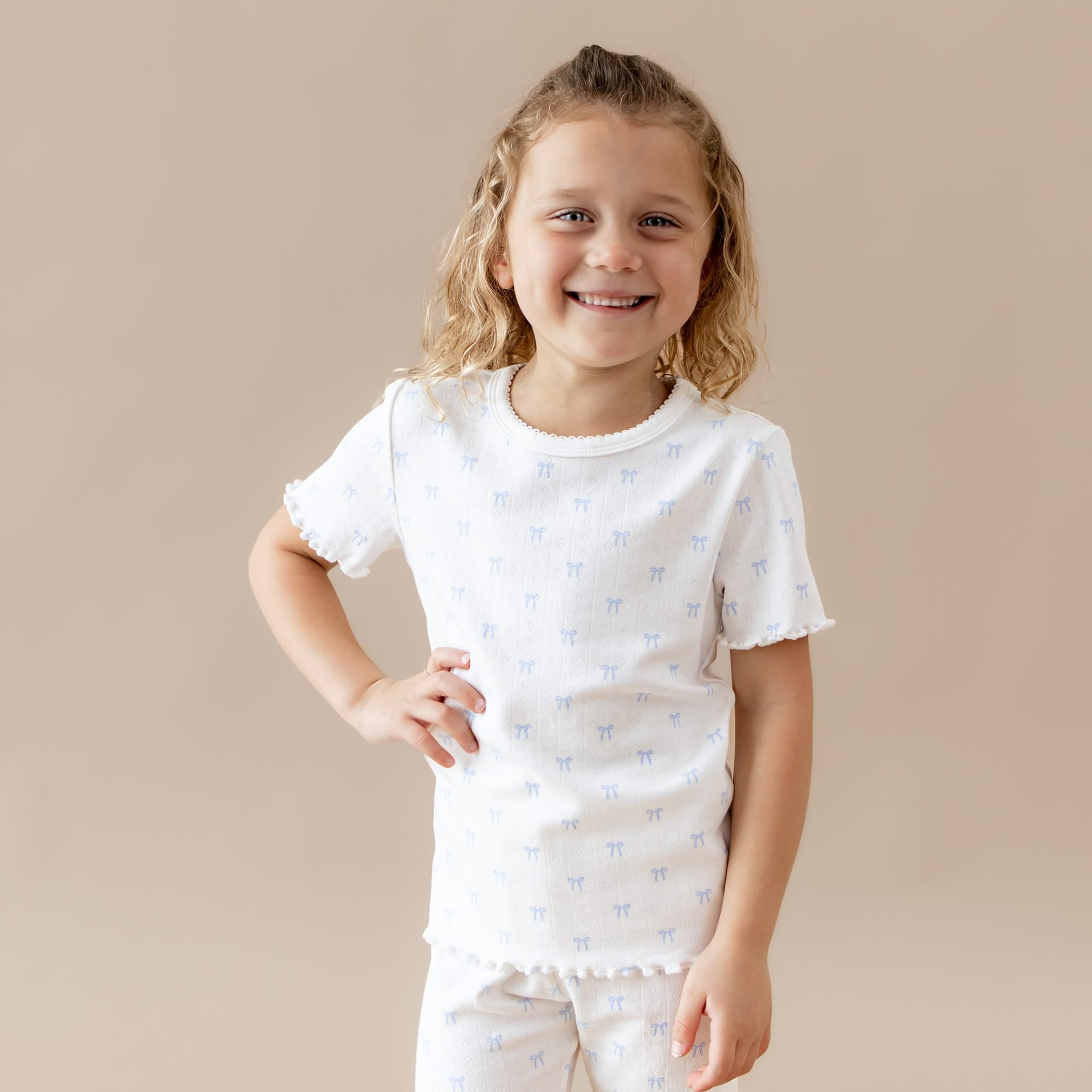 Young girl wearing a white t-shirt with small blue bow patterns on a beige background