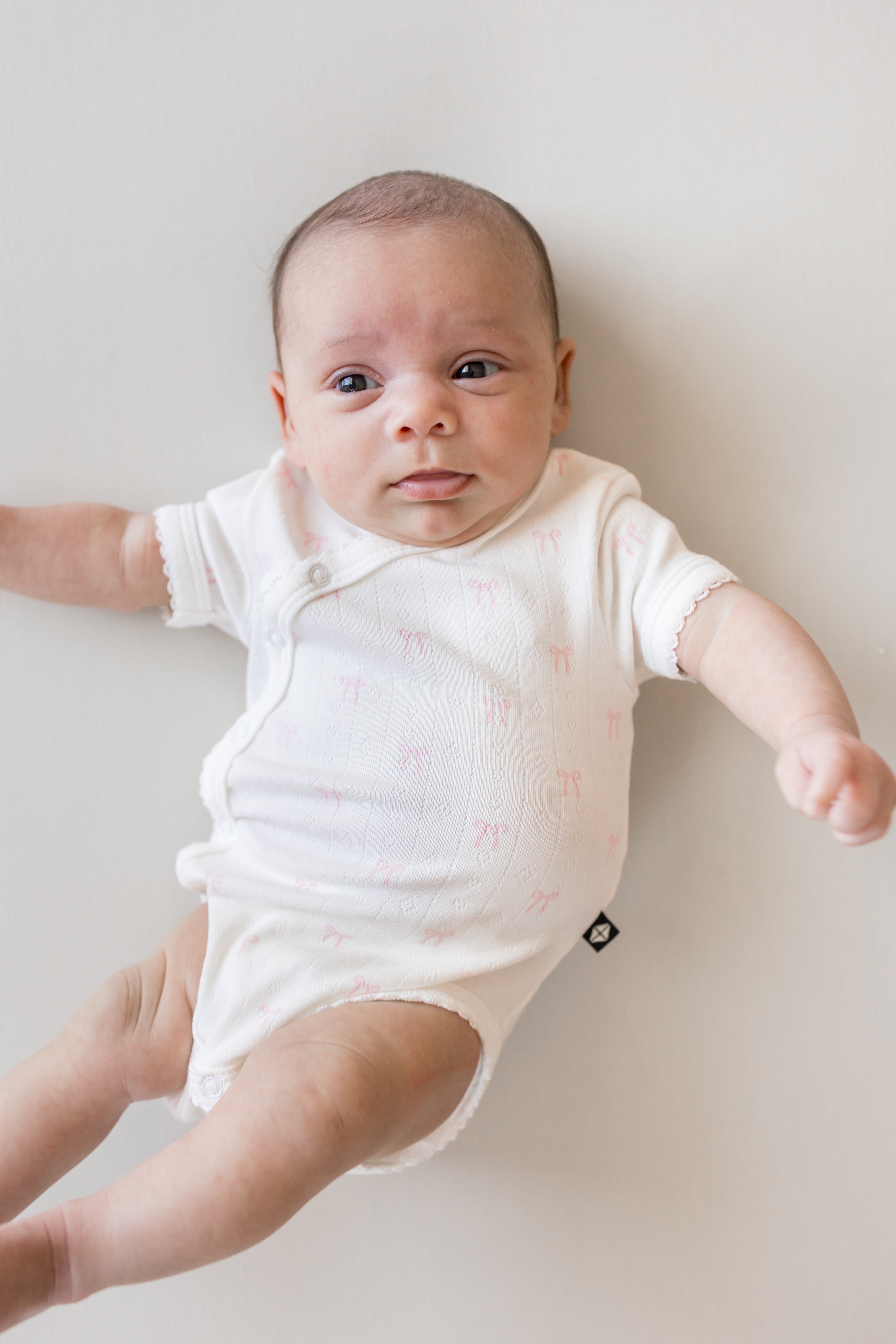 Baby wearing Pointelle Kimono Bodysuit in Sweet Pink Bow print on a beige background