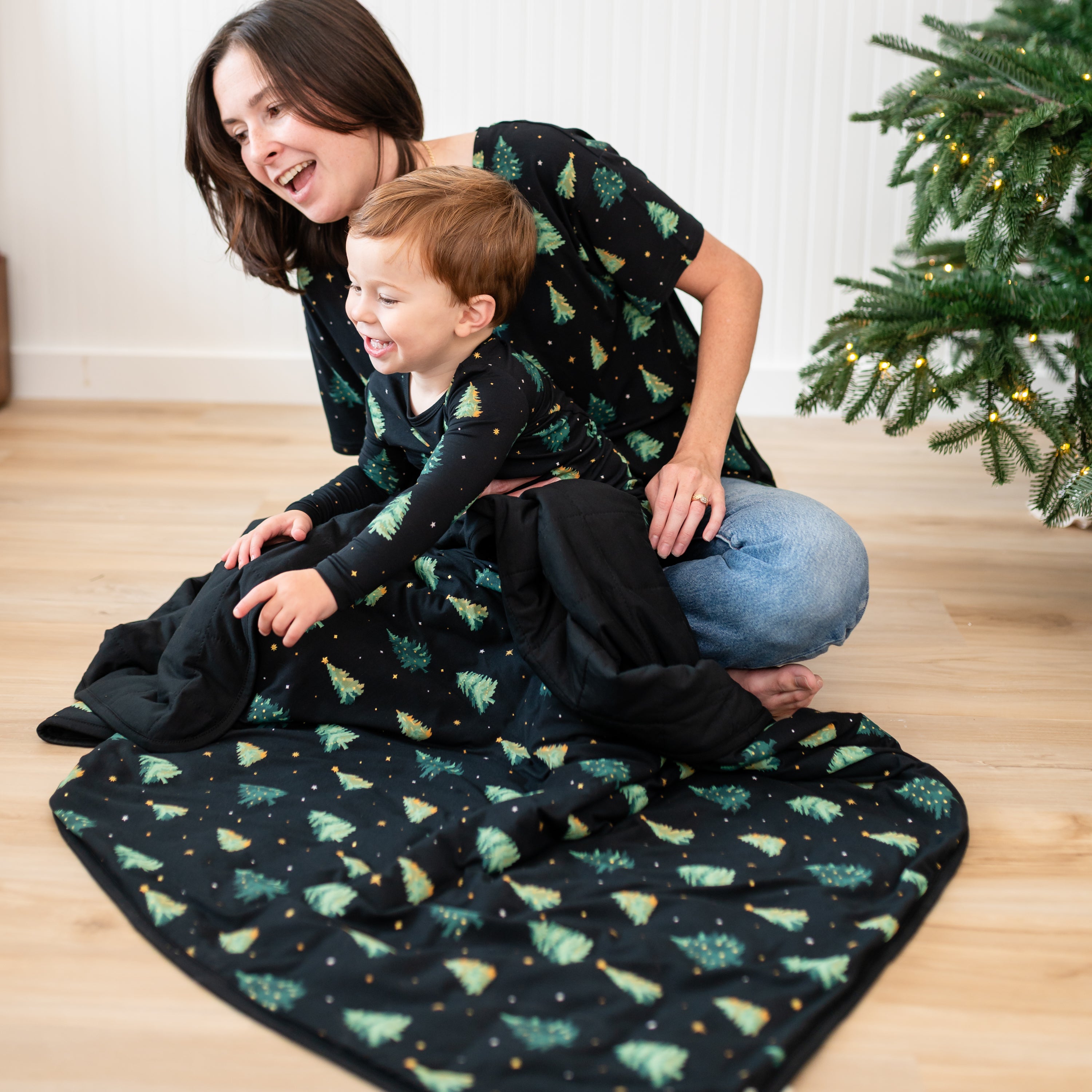 Mother and son sitting on the floor with the Toddler Blanket in Twinkle Tree 1.0 overtop of their legs