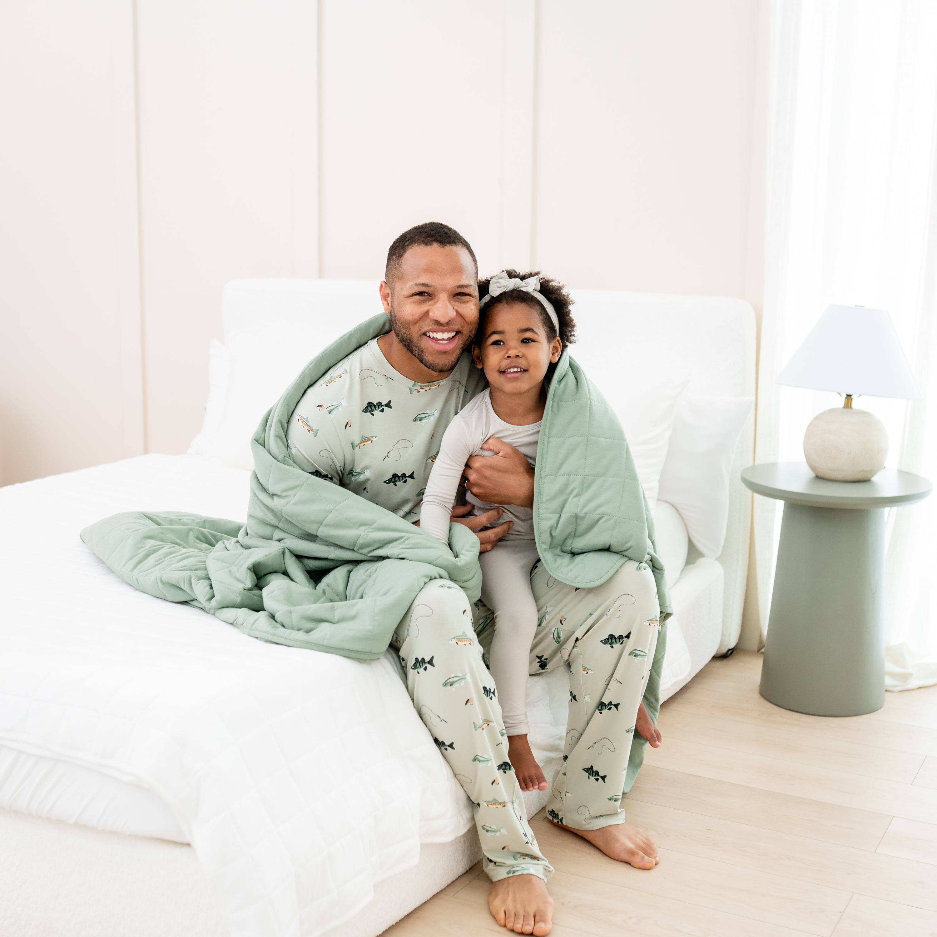 Man in Fishing jogger set holding toddler in oat long sleeve pajamas wrapped in Adult Quilted Blanket in Thyme 2.5