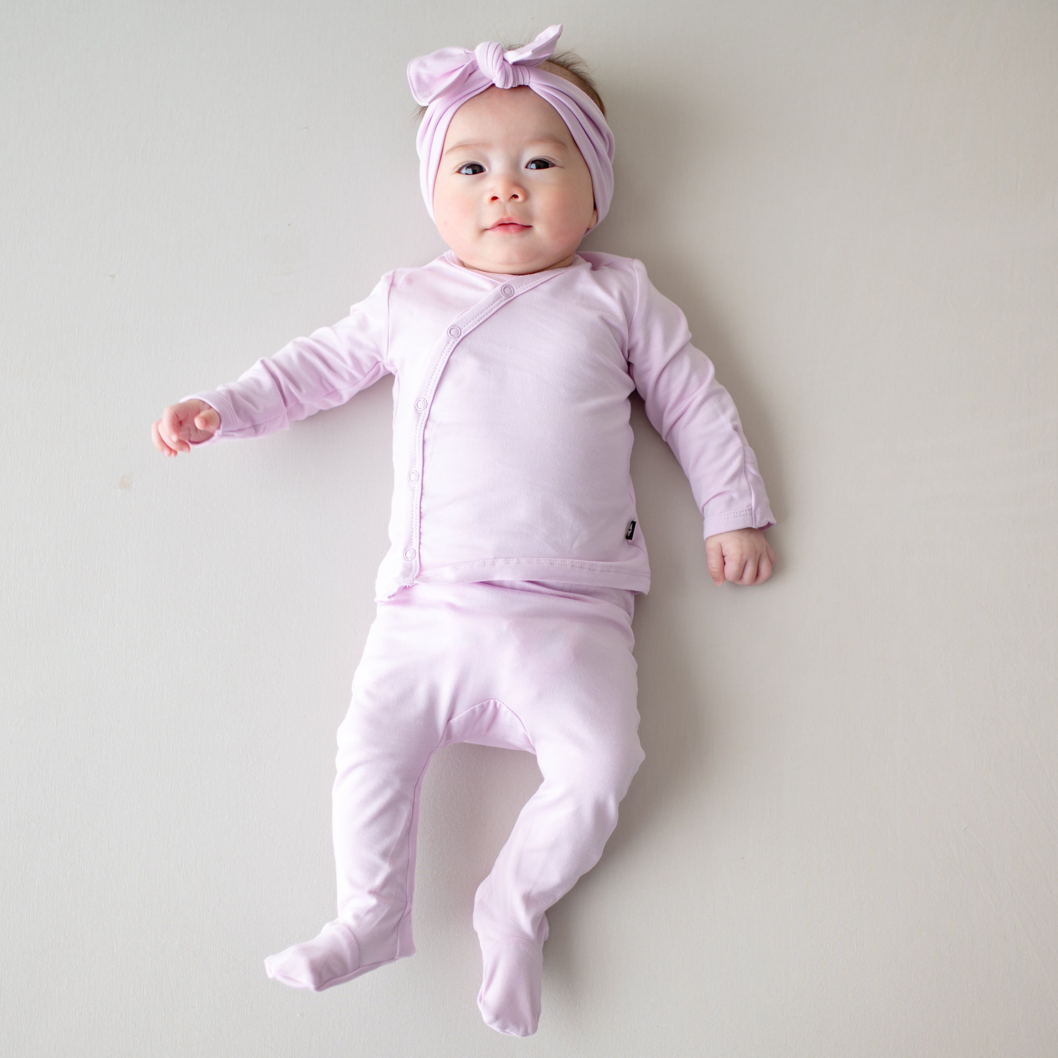 Newborn laying on a light neutral surface wearing the Take Me Home Set with Bow in Thistle
