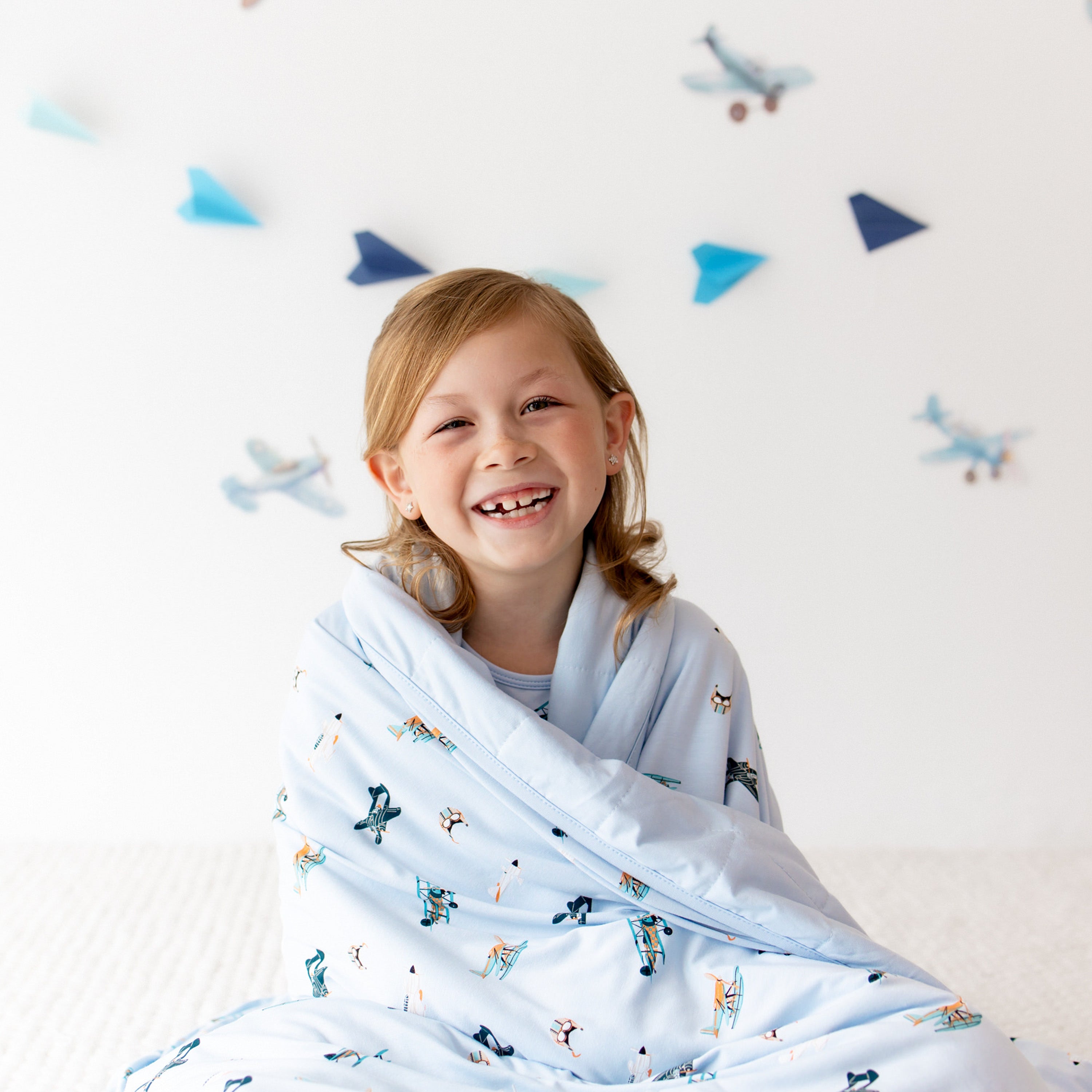 Close up of smiling girl sitting on the floor with he Youth Blanket in Take Off 1.0 wrapped around her