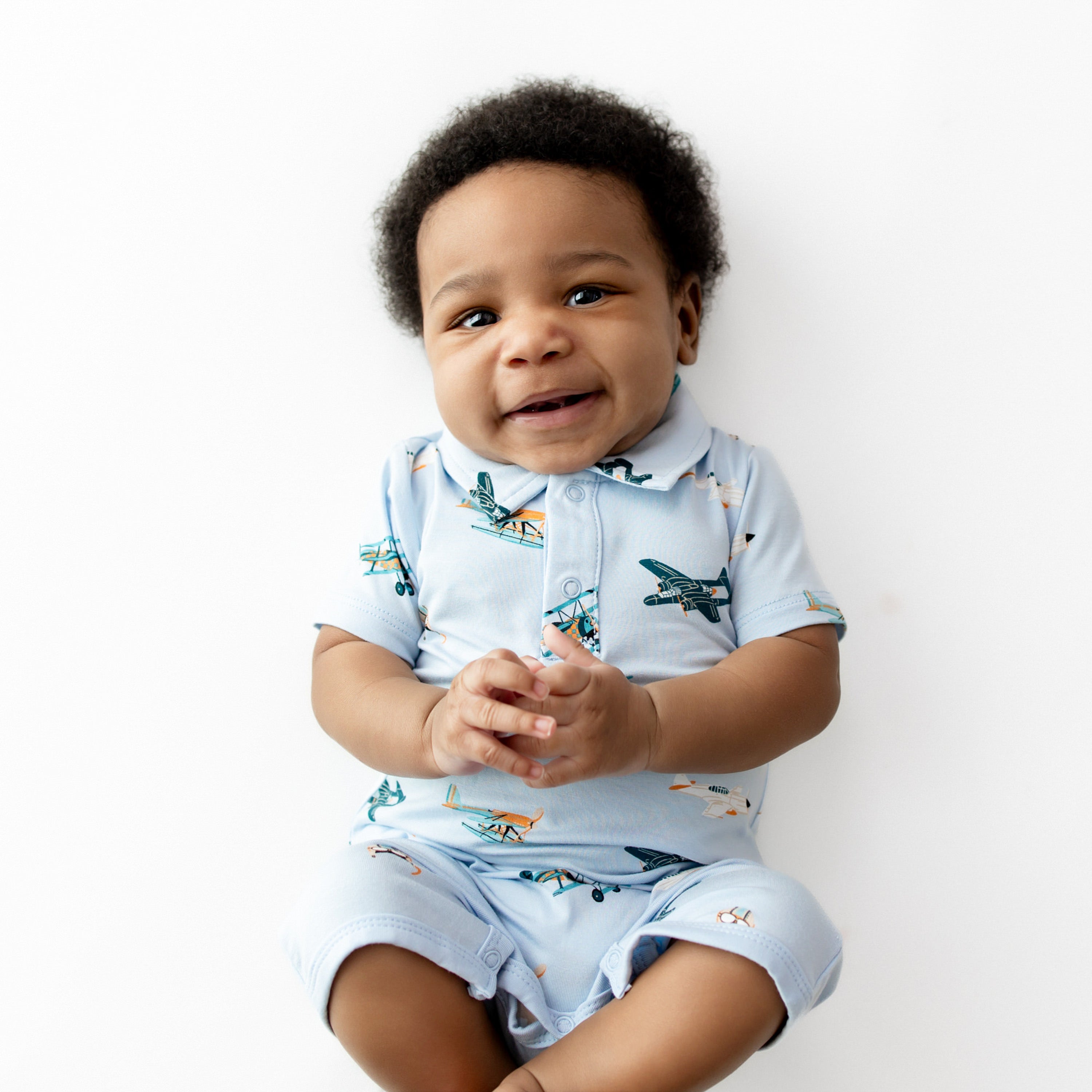 Smiling infant laying on a white surface wearing the Polo Shortall in Take Off