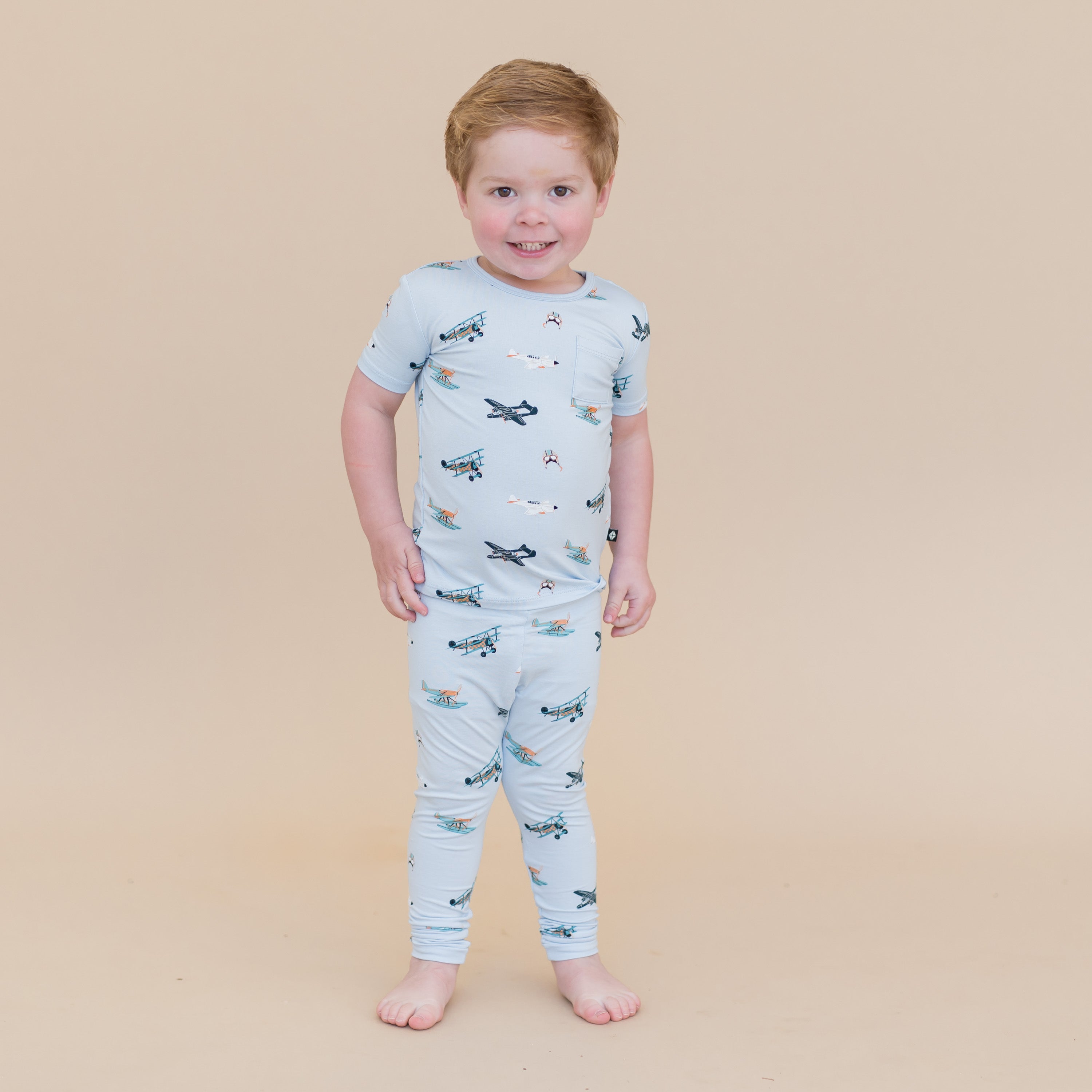 Young boy standing in front of a light taupe background wearing the Short Sleeve with Pants Pajamas in Take Off