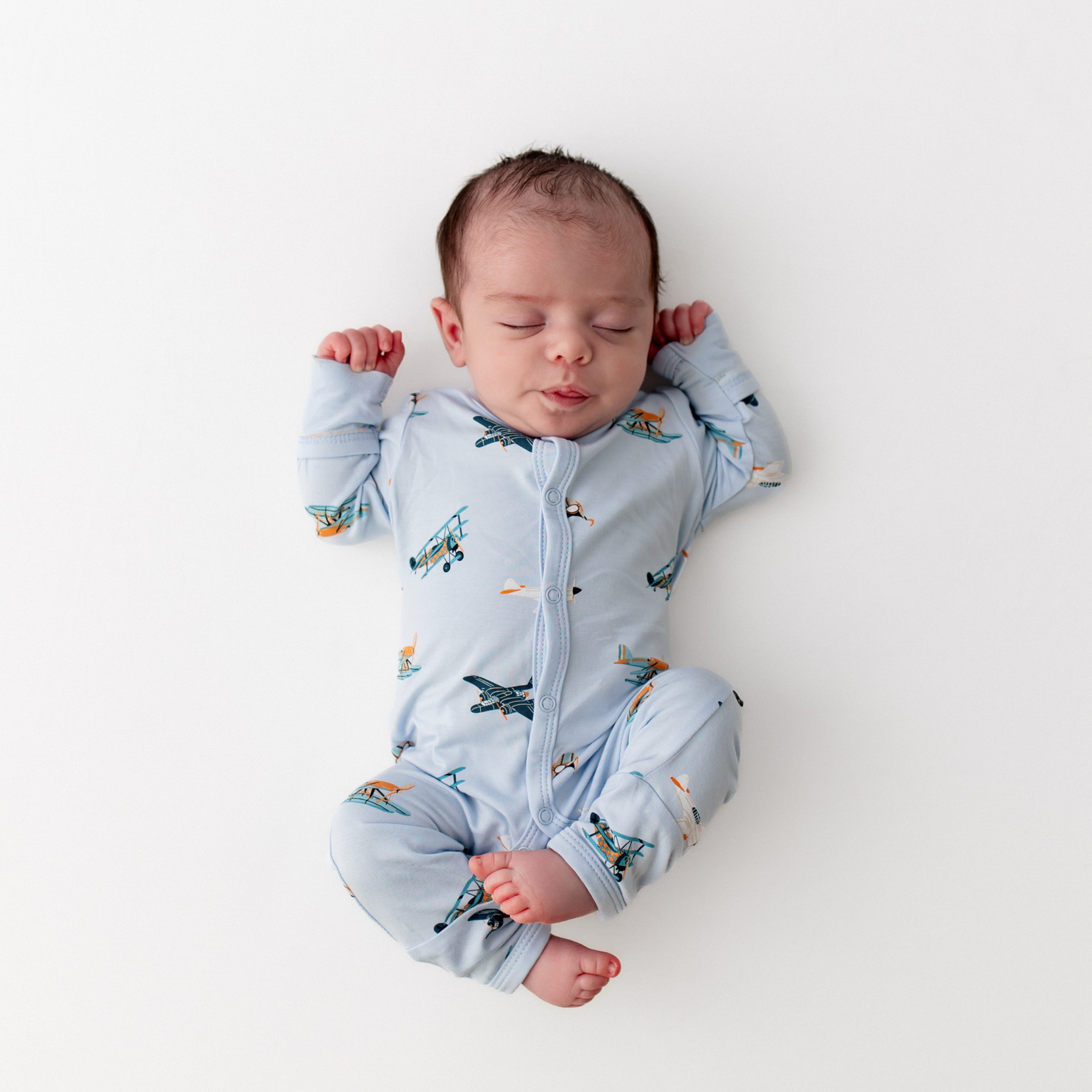 Sleeping newborn laying on a white surface wearing the Romper in Take Off