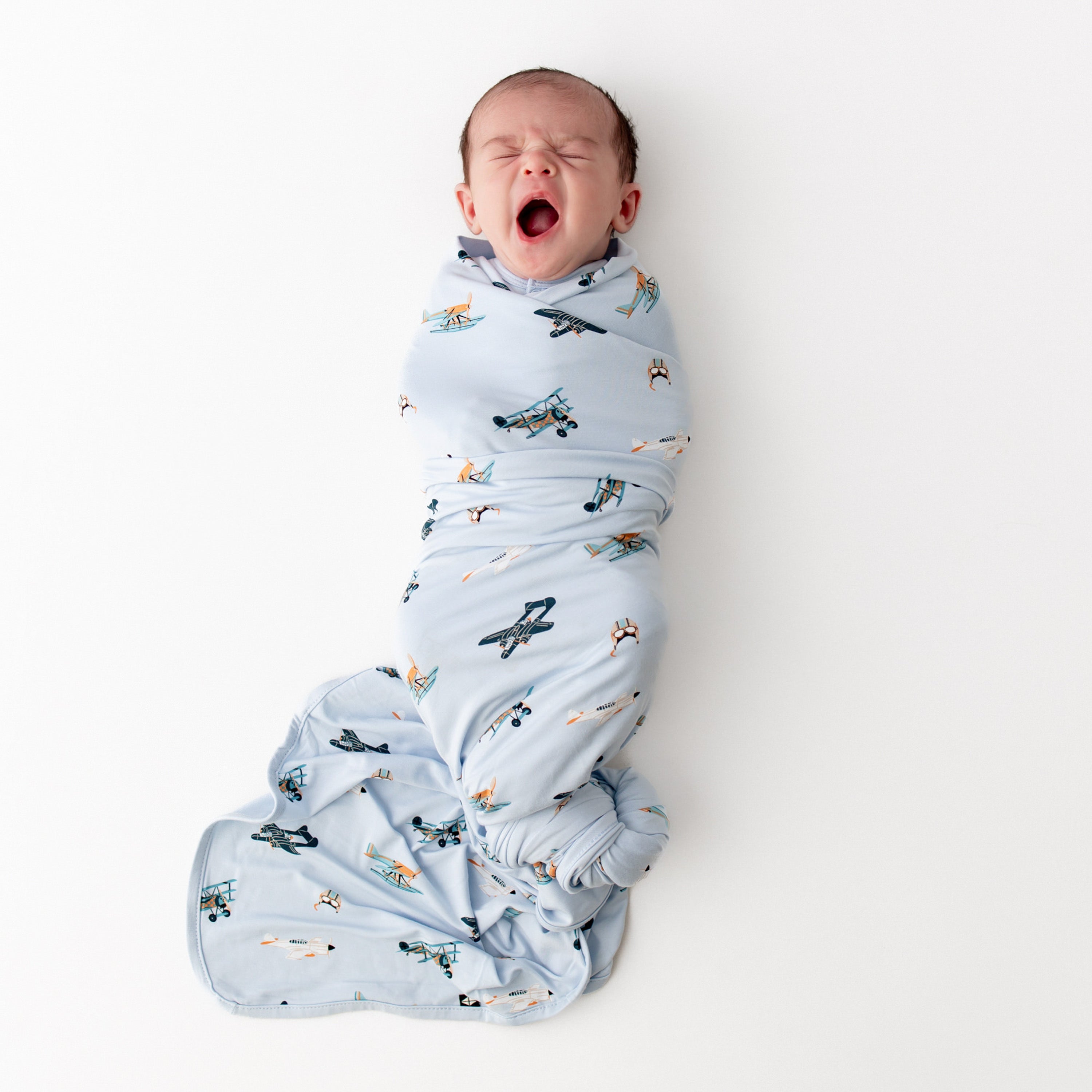 Yawning newborn swaddled in the Swaddle Blanket in Take Off