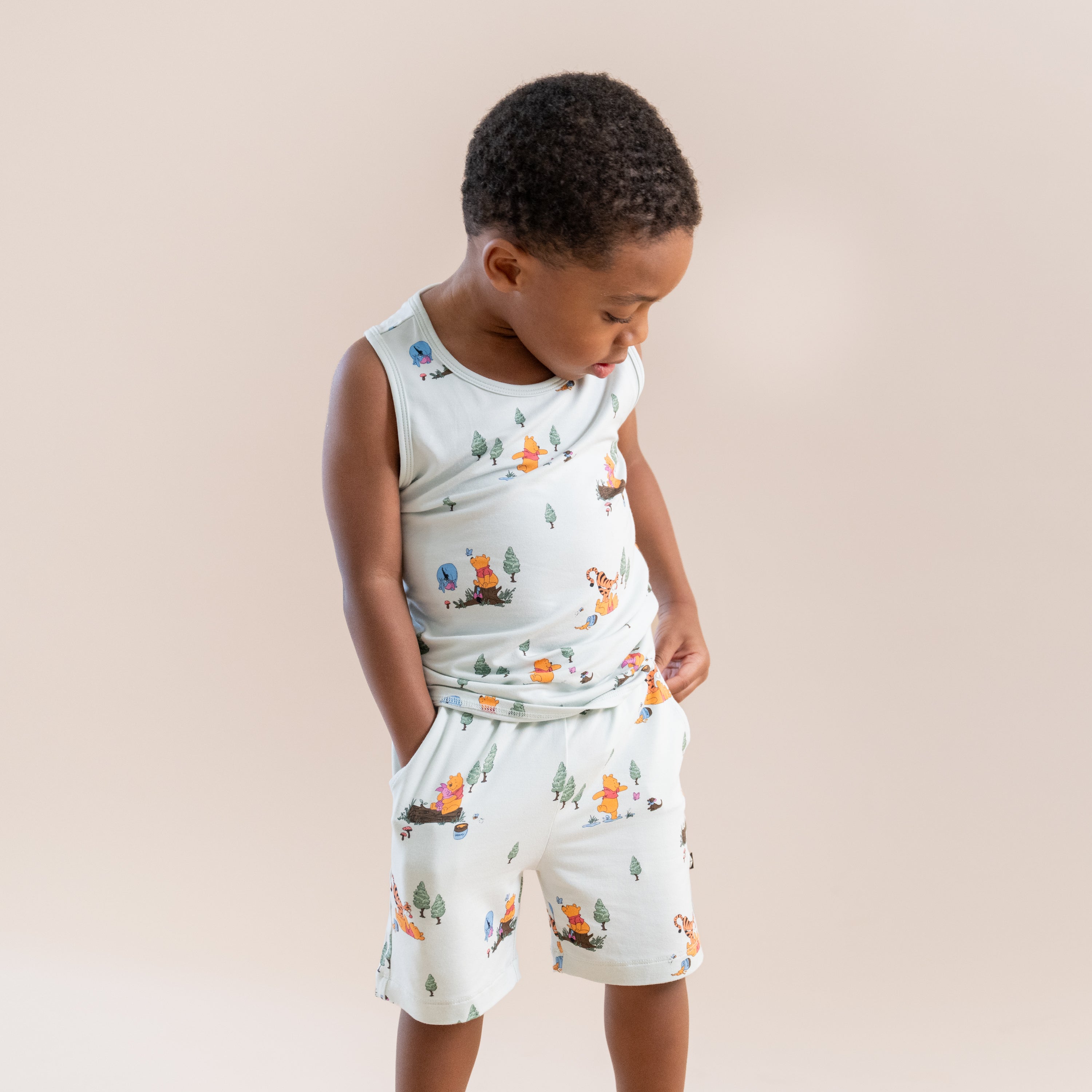 Boy standing wearing the Toddler Tank Top in Winnie the Pooh Hundred Acre Wood with matching drawstring shorts with one hand in the pocket