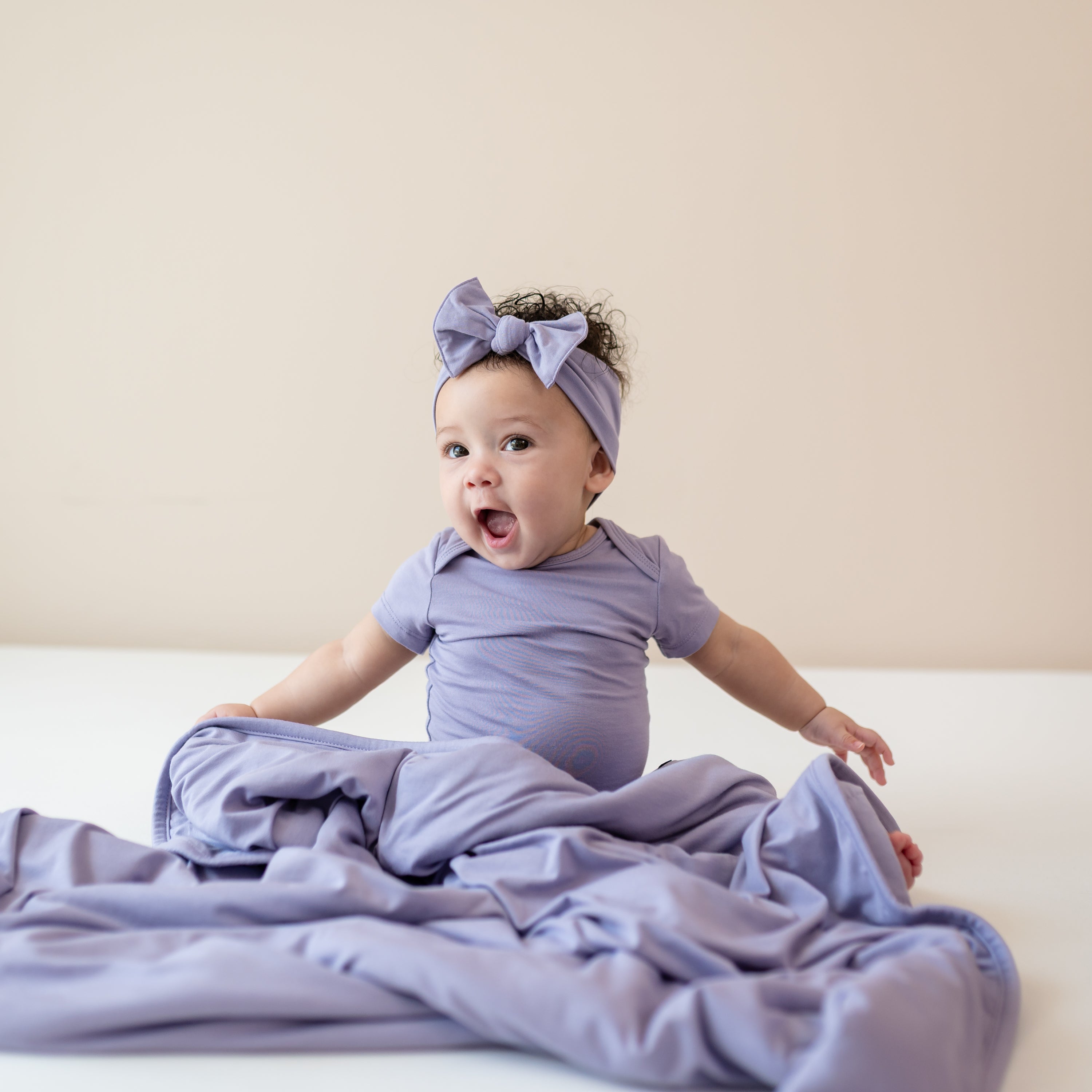 Baby sitting with Baby Blanket in Taro 1.0 wearing matching bodysuit and bow