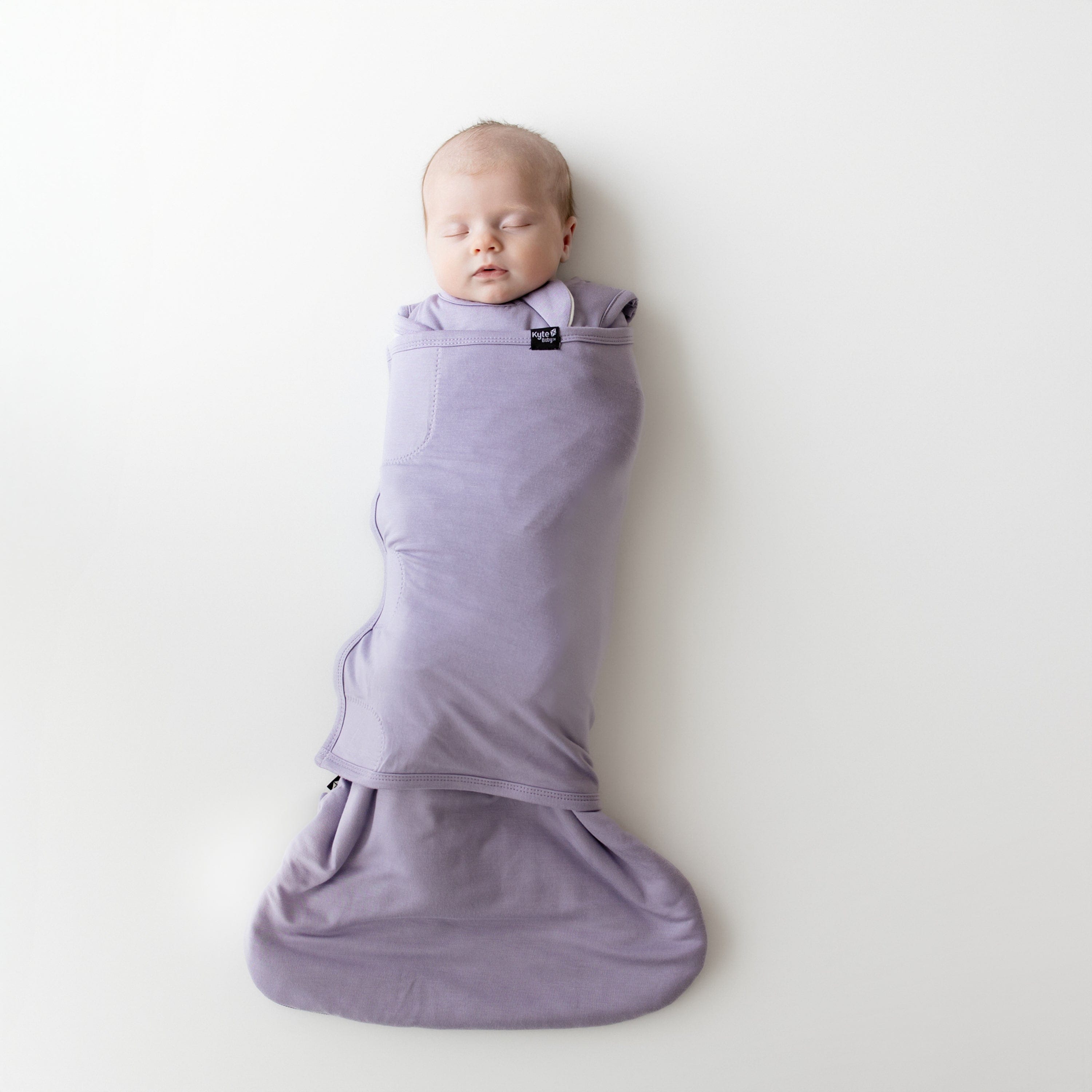 Baby swaddled in a purple swaddler on a white background