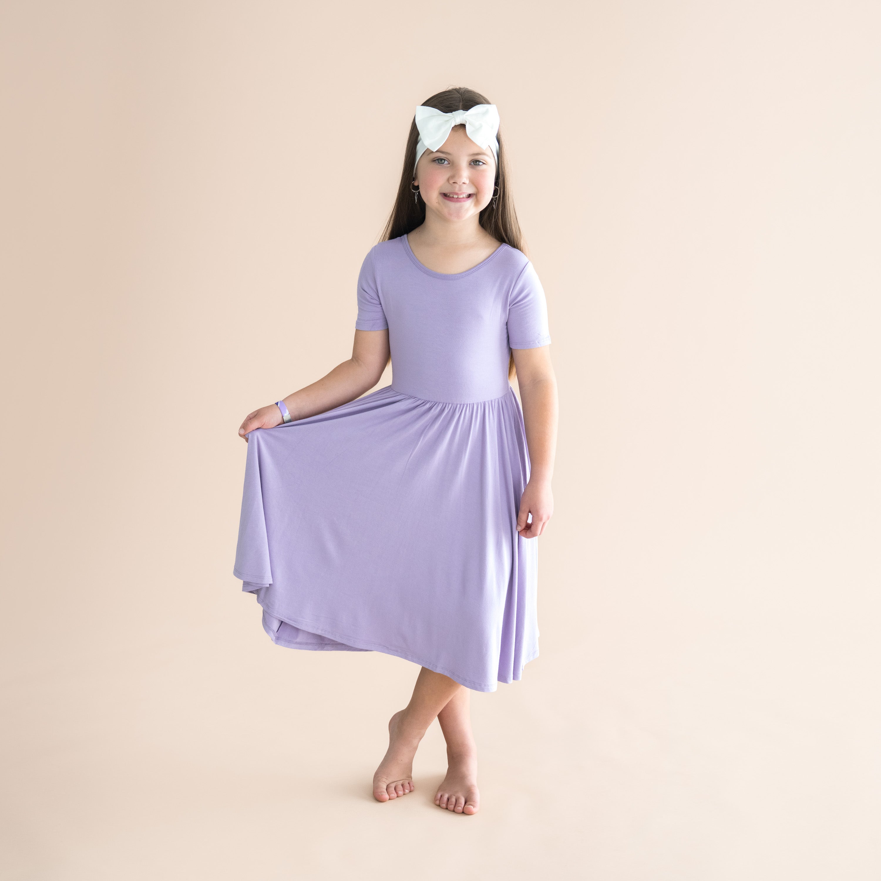 Young girl wearing a light purple dress and headband on a beige background