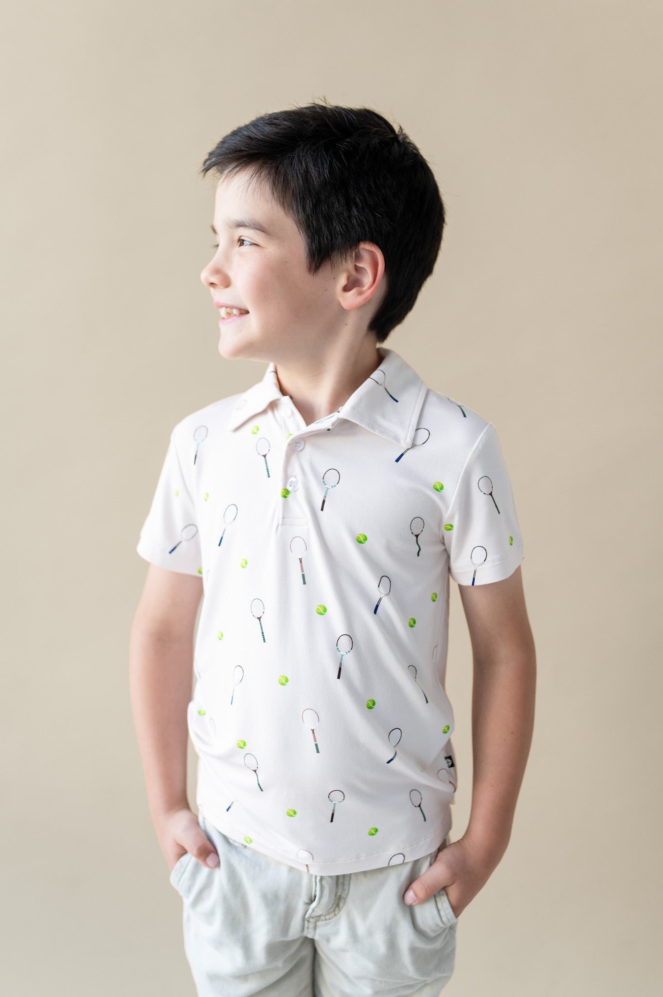 Young boy wearing a white shirt with tennis racket pattern against a beige background