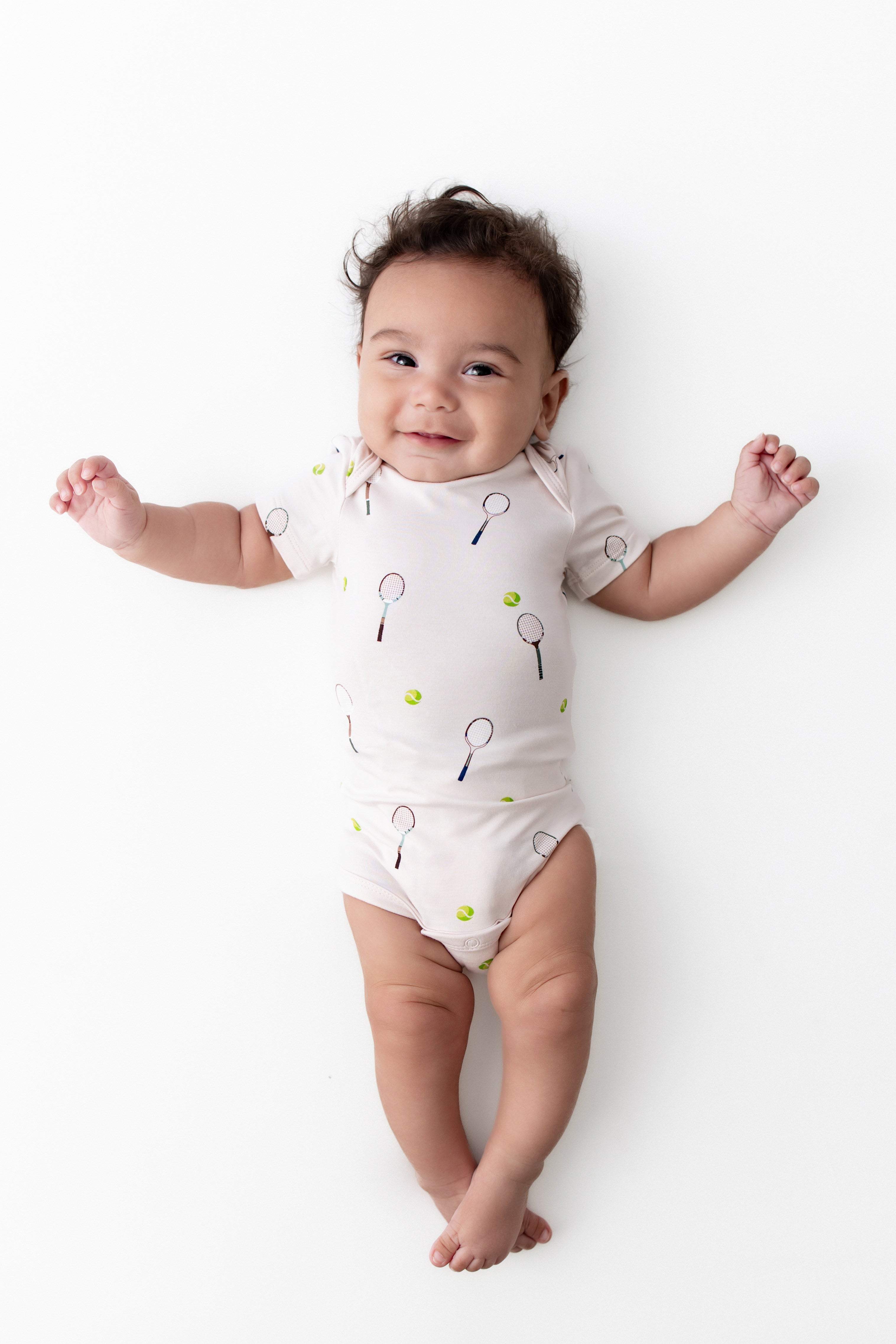 Baby wearing a onesie with tennis racket prints on a white background