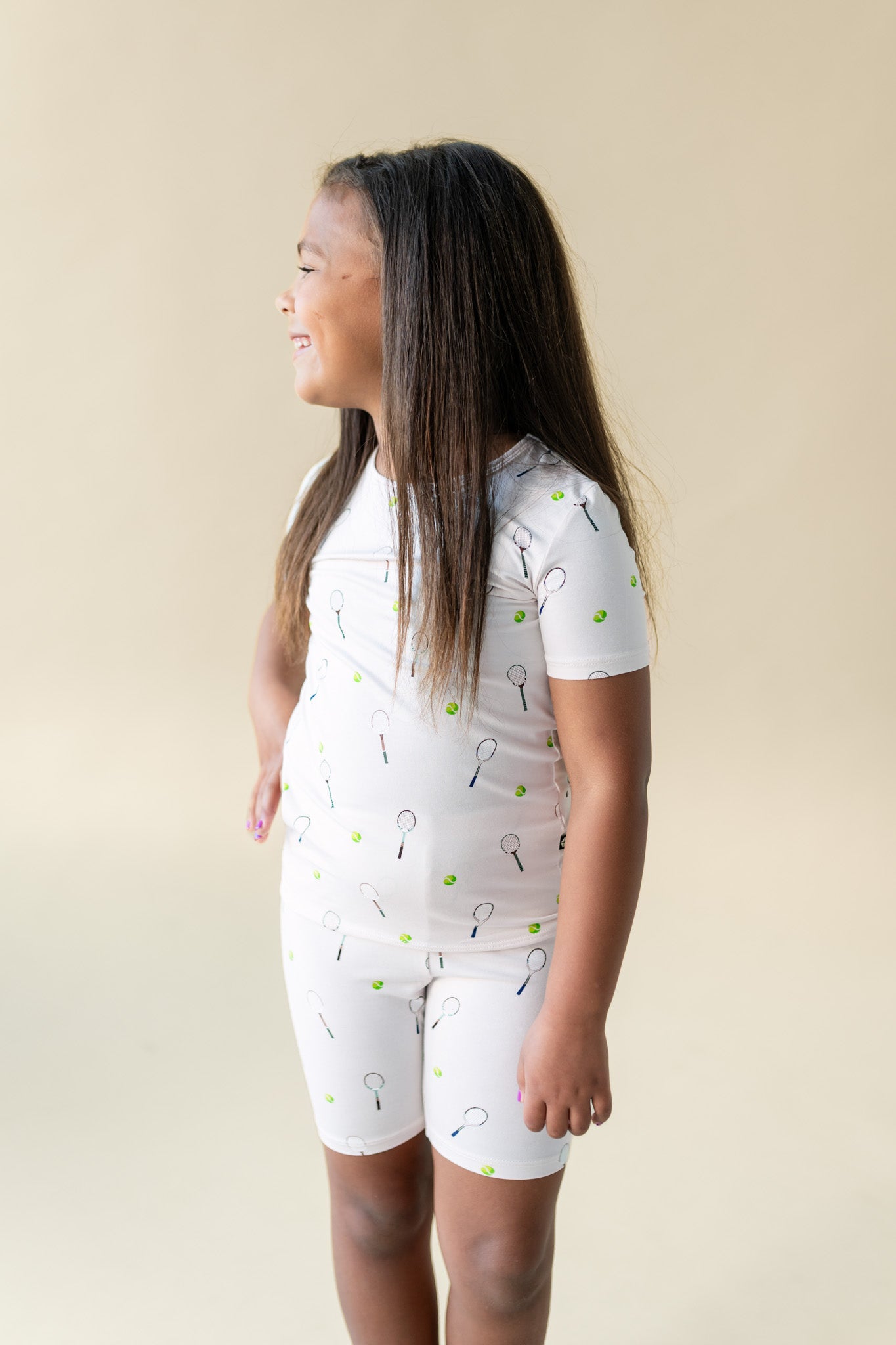 Young girl wearing a white pajama set with a tennis pattern on a beige background