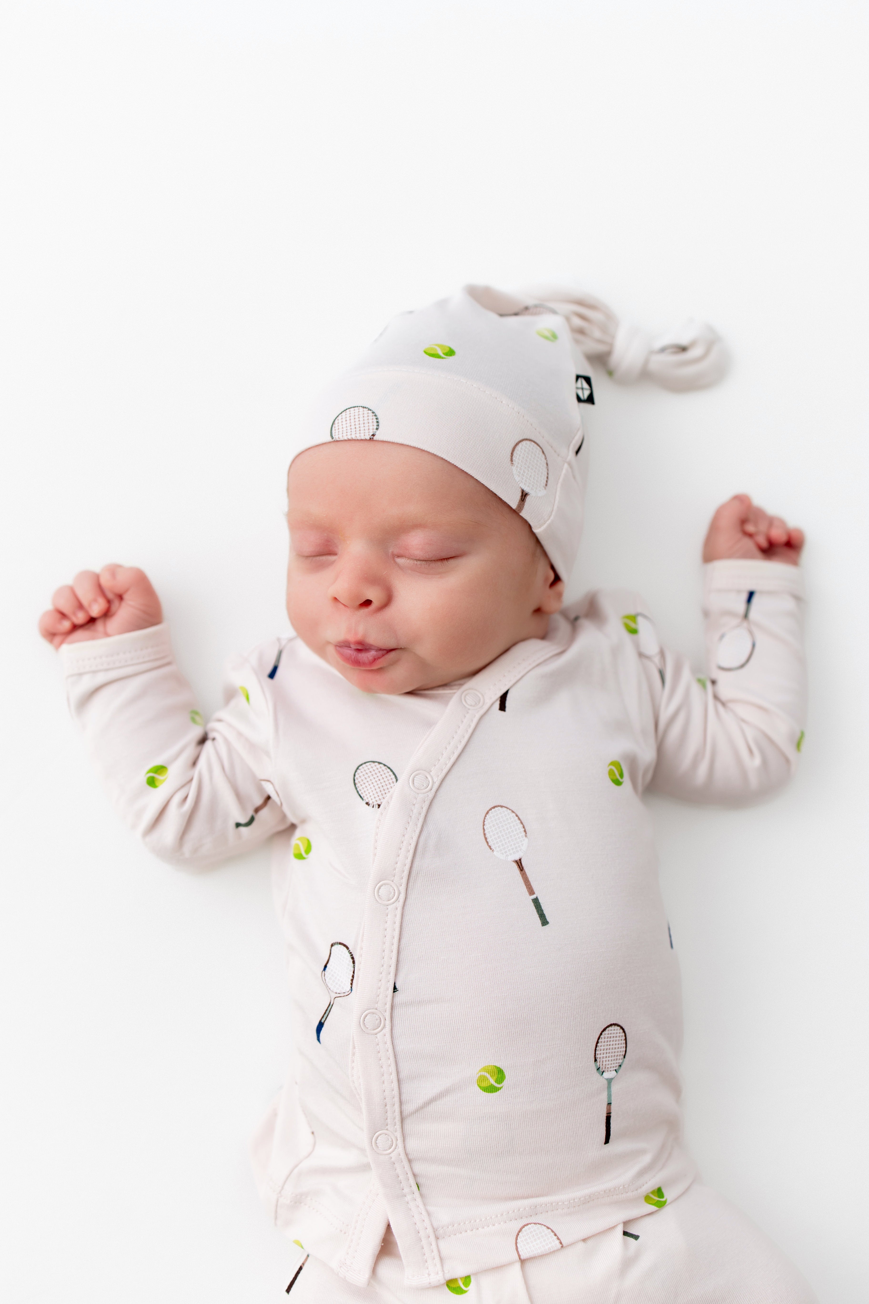 Newborn baby wearing a white outfit with tennis patterns on a white background