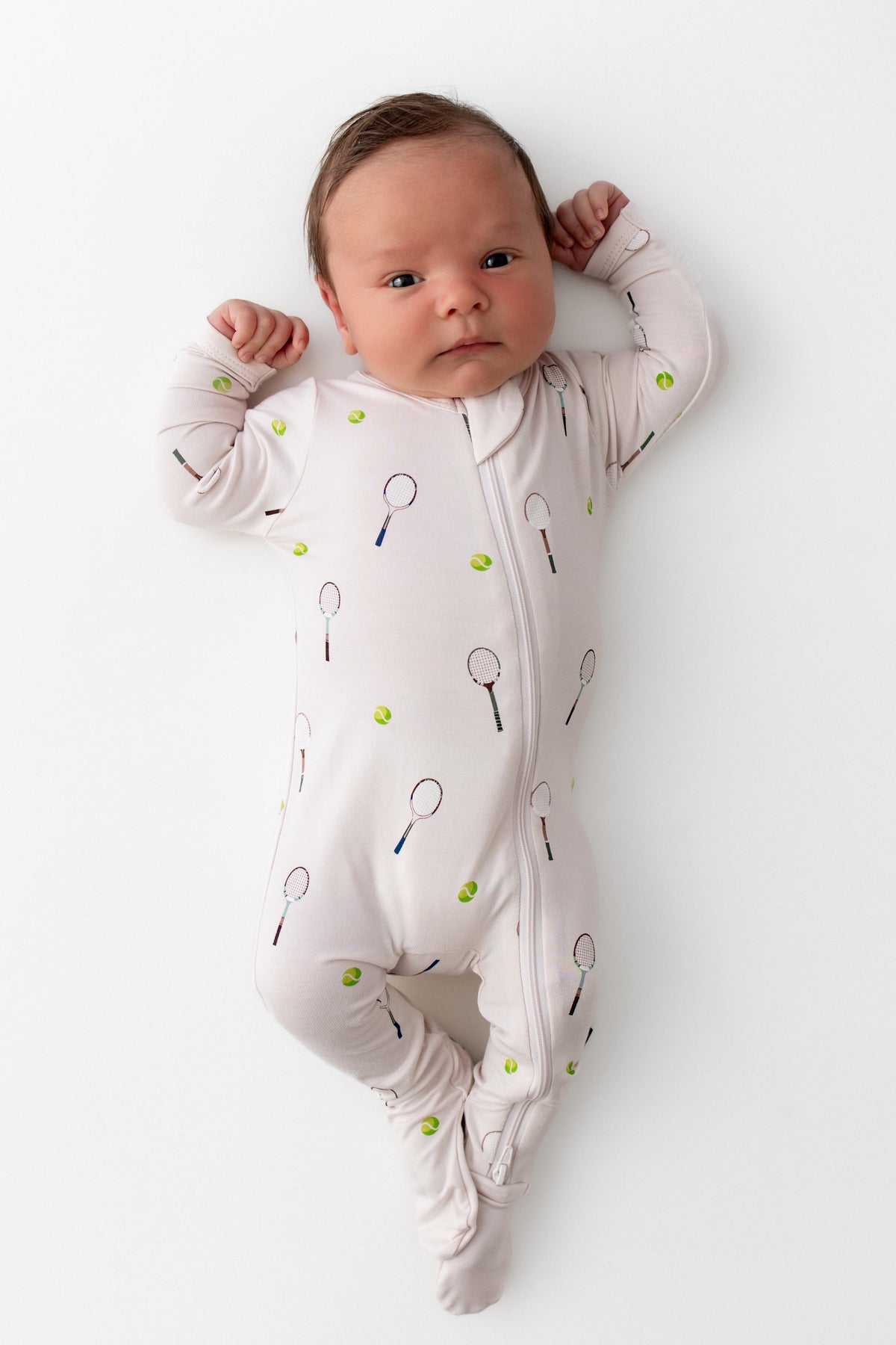 Newborn baby wearing a onesie with tennis racket and ball pattern on a white background
