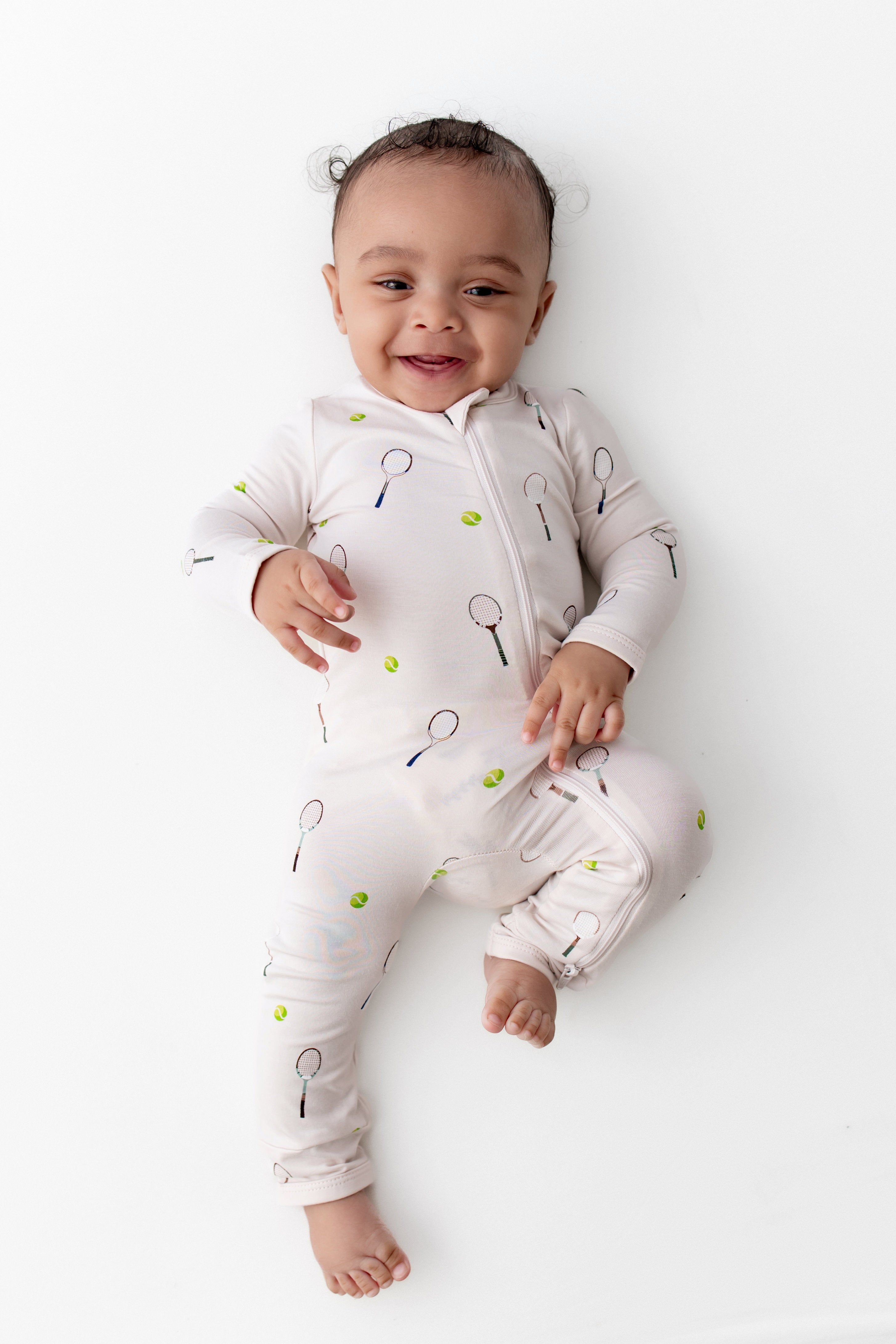 Baby wearing a white onesie with tennis patterns on a white background