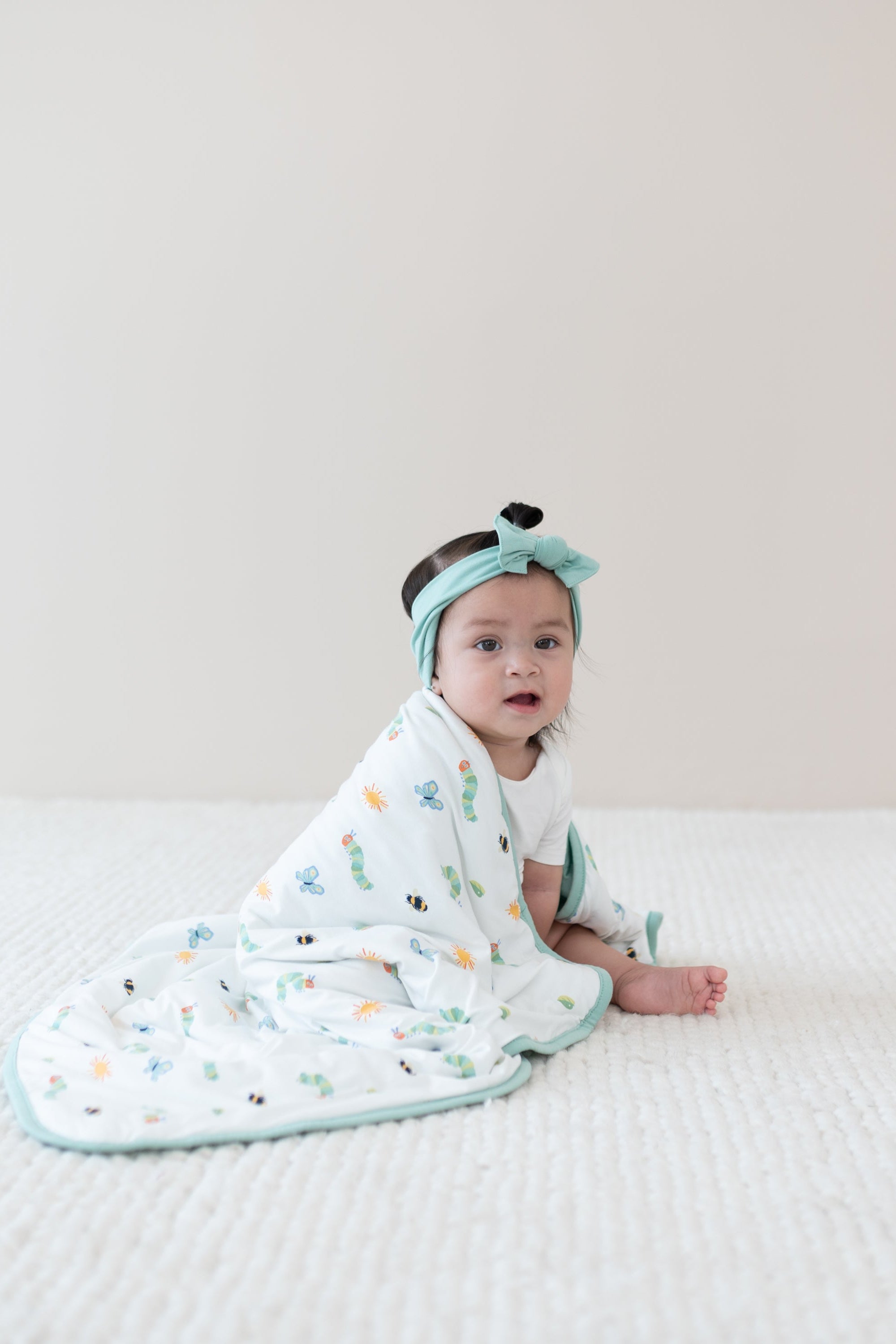 Baby sitting wrapped with Baby Blanket in The Very Hungry Caterpillar™ and Friends 1.0 around shoulders