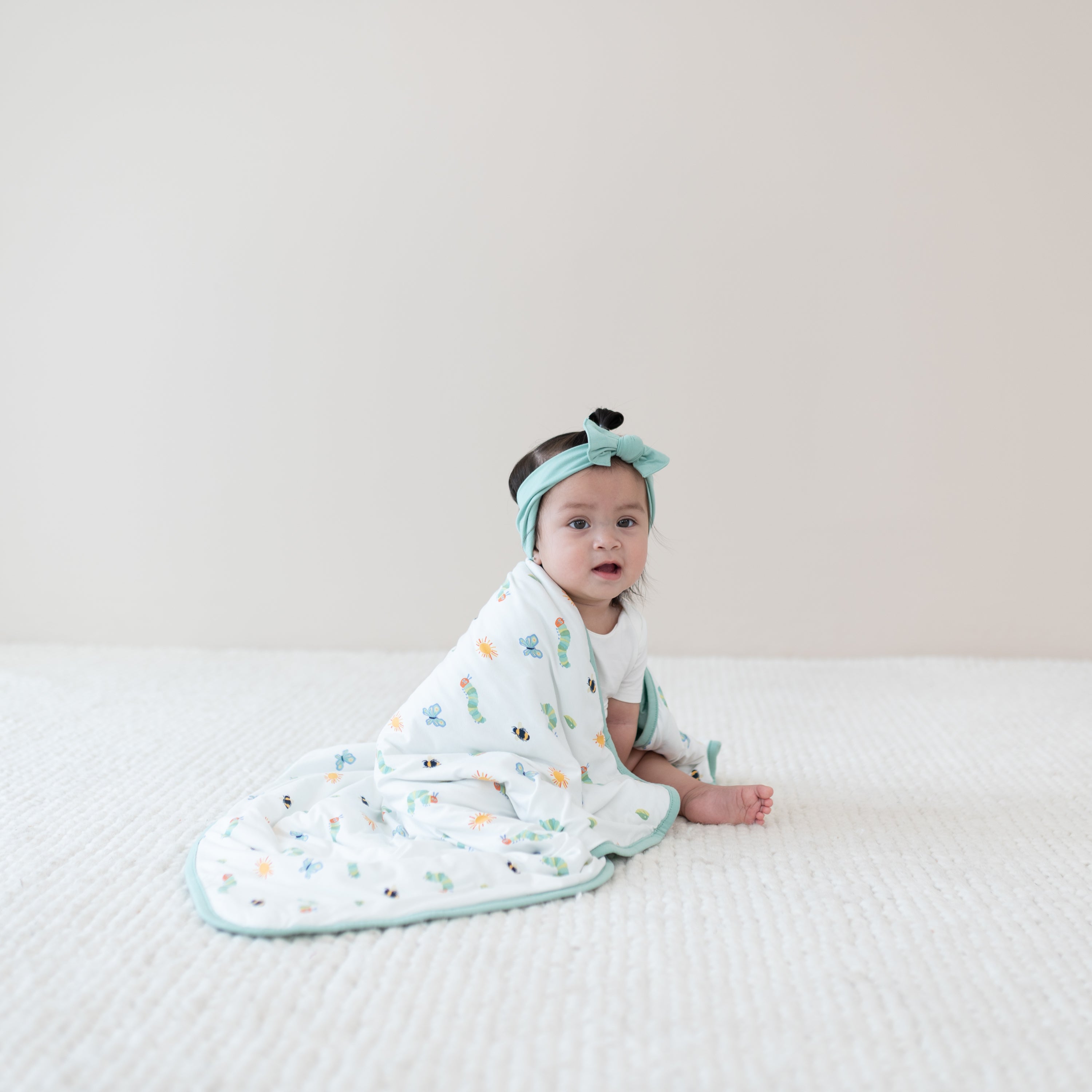 Baby sitting wrapped with Baby Blanket in The Very Hungry Caterpillar™ and Friends 1.0 around shoulders