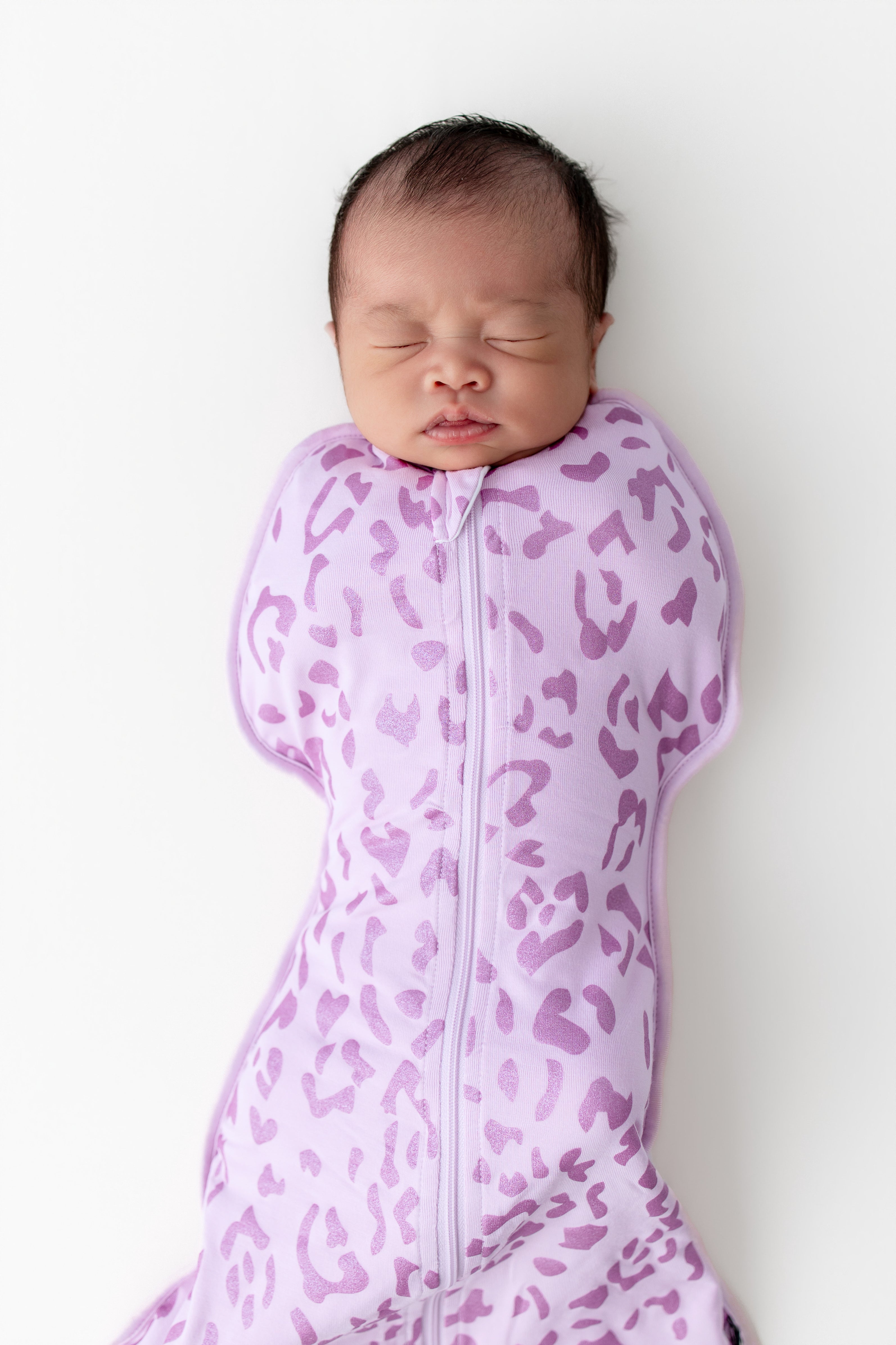 Baby sleeping in a Thistle Leopard print Swaddle bag on a white background