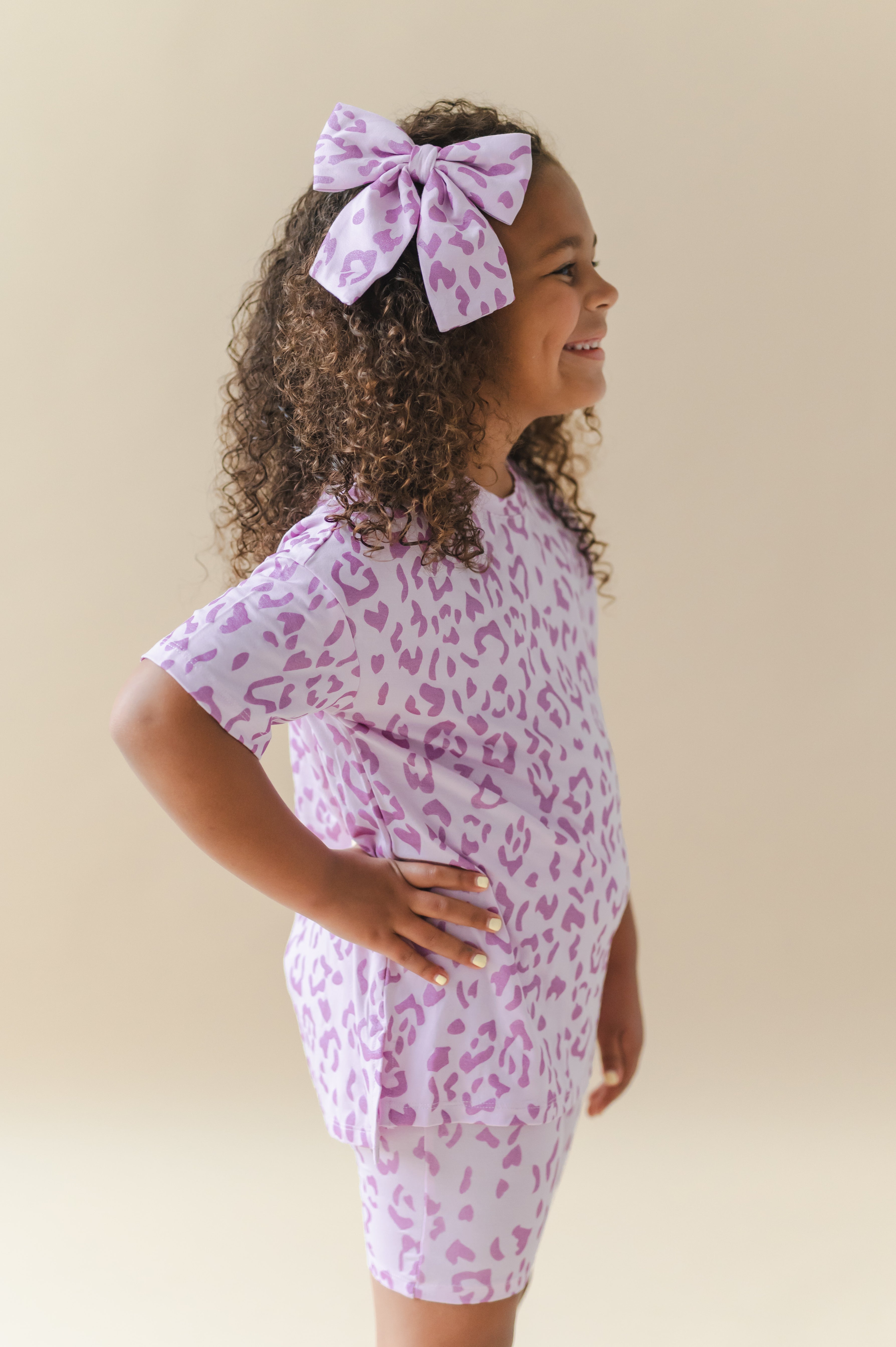 Side pose of child wearing Large alligator clip bow and toddler biker short set in Thistle Leopard print on a beige background