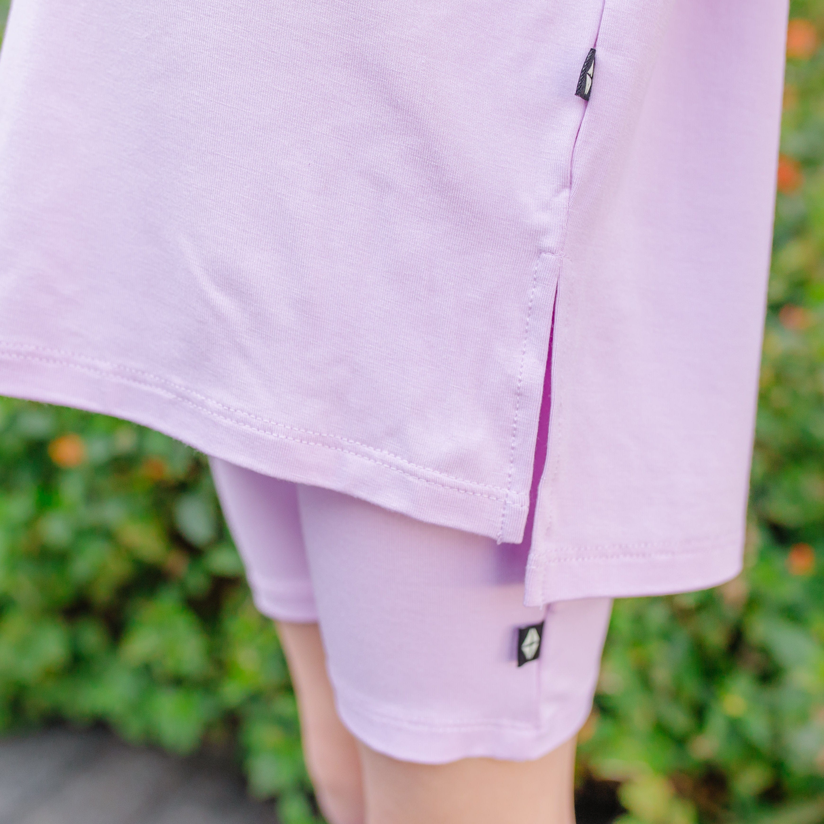 Close-up of a child wearing light purple biker shorts and oversized tee with a blurred green background