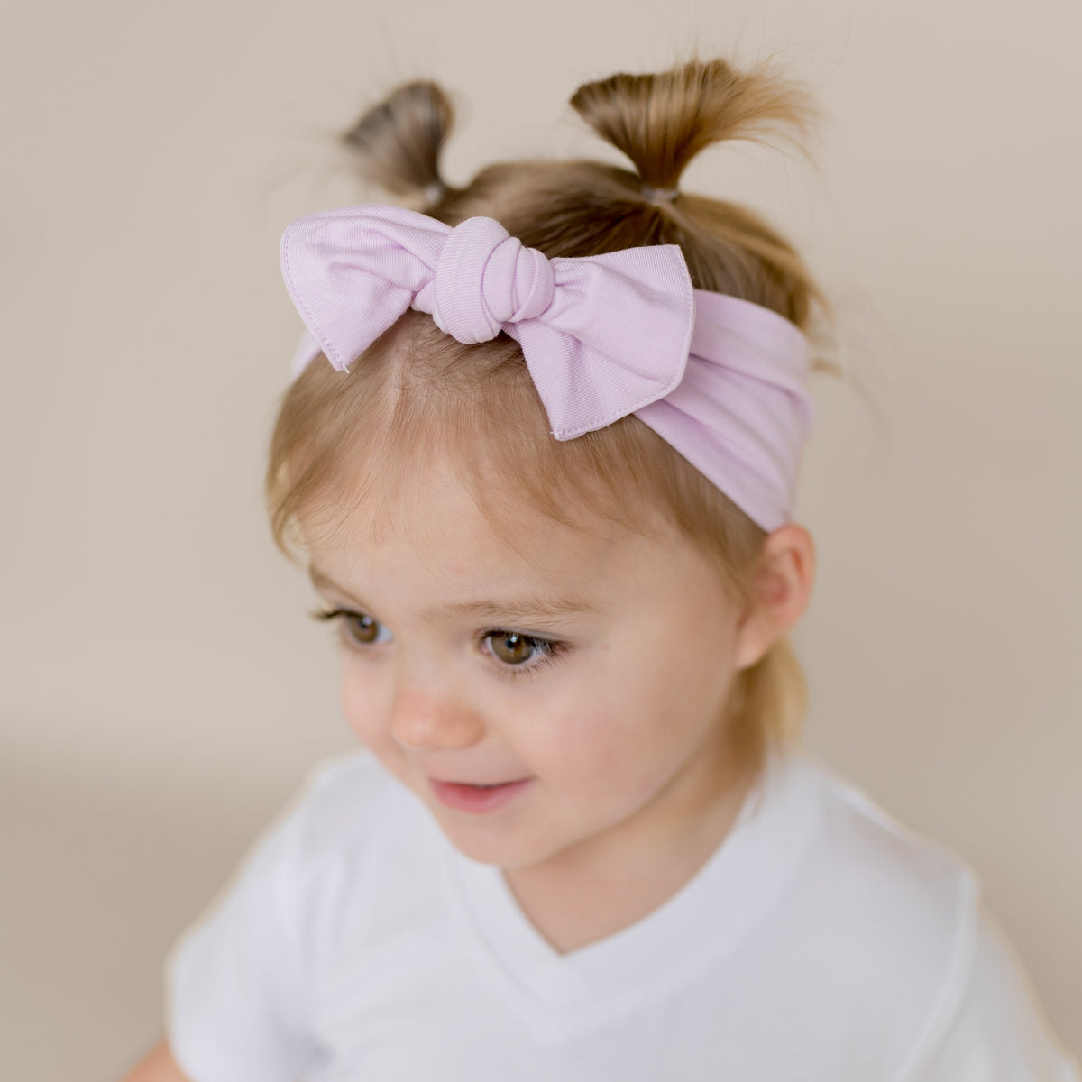 Knotted Bow Headband in Thistle shown on a young girl model wearing a white v-neck shirt